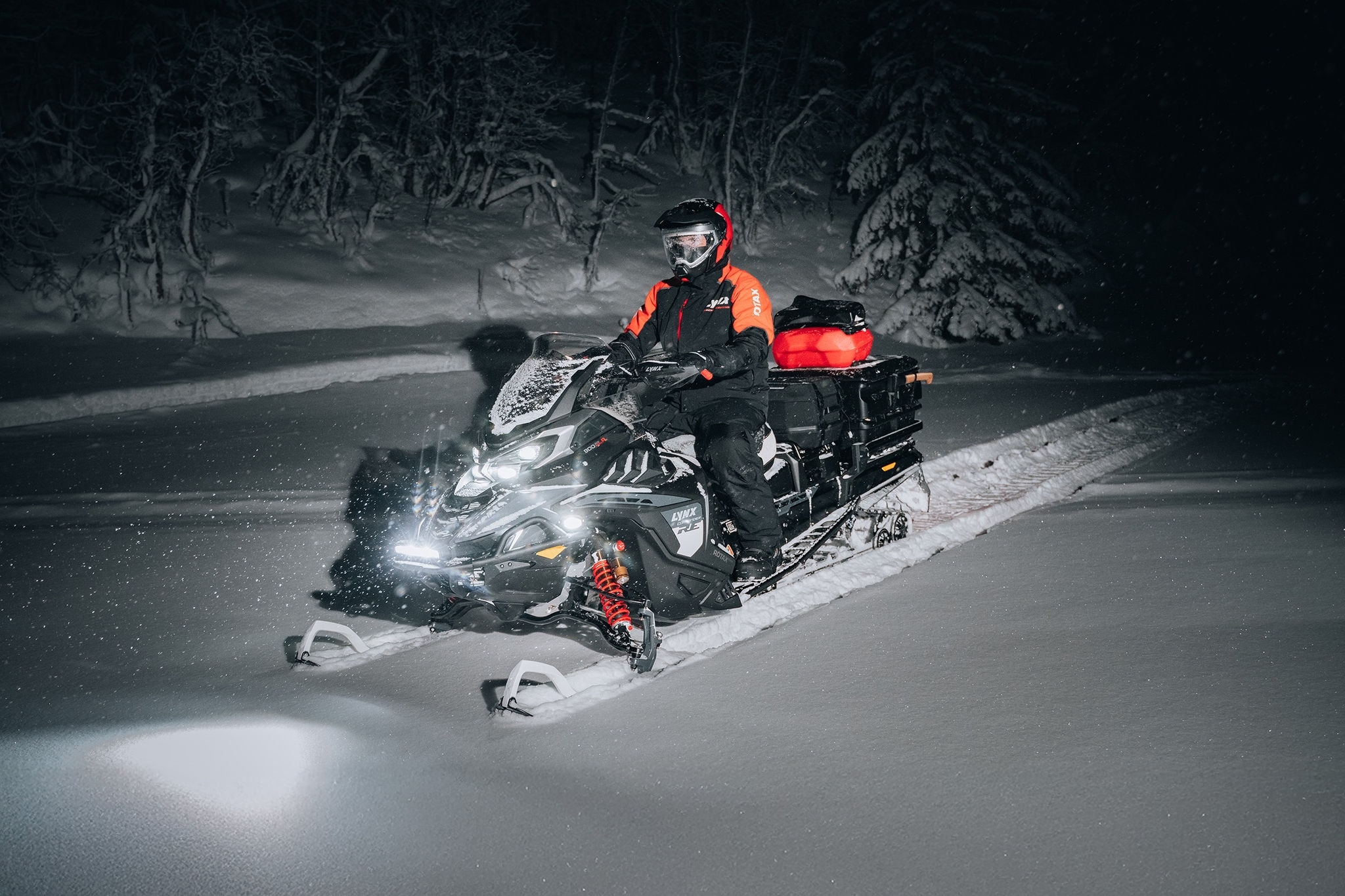 Förare kör en 2027 Lynx Commander RE snöskoter på natten med last