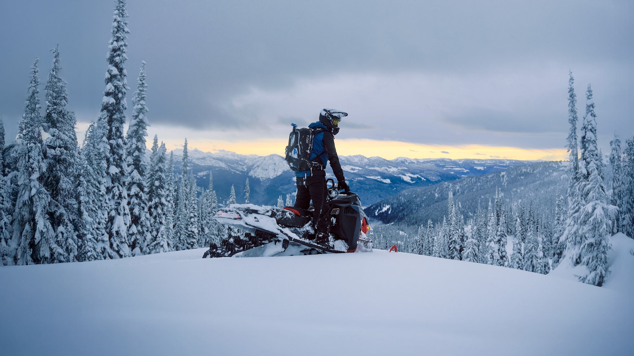 Man står på en 2027 Lynx Shredder snöskoter på toppen av ett berg