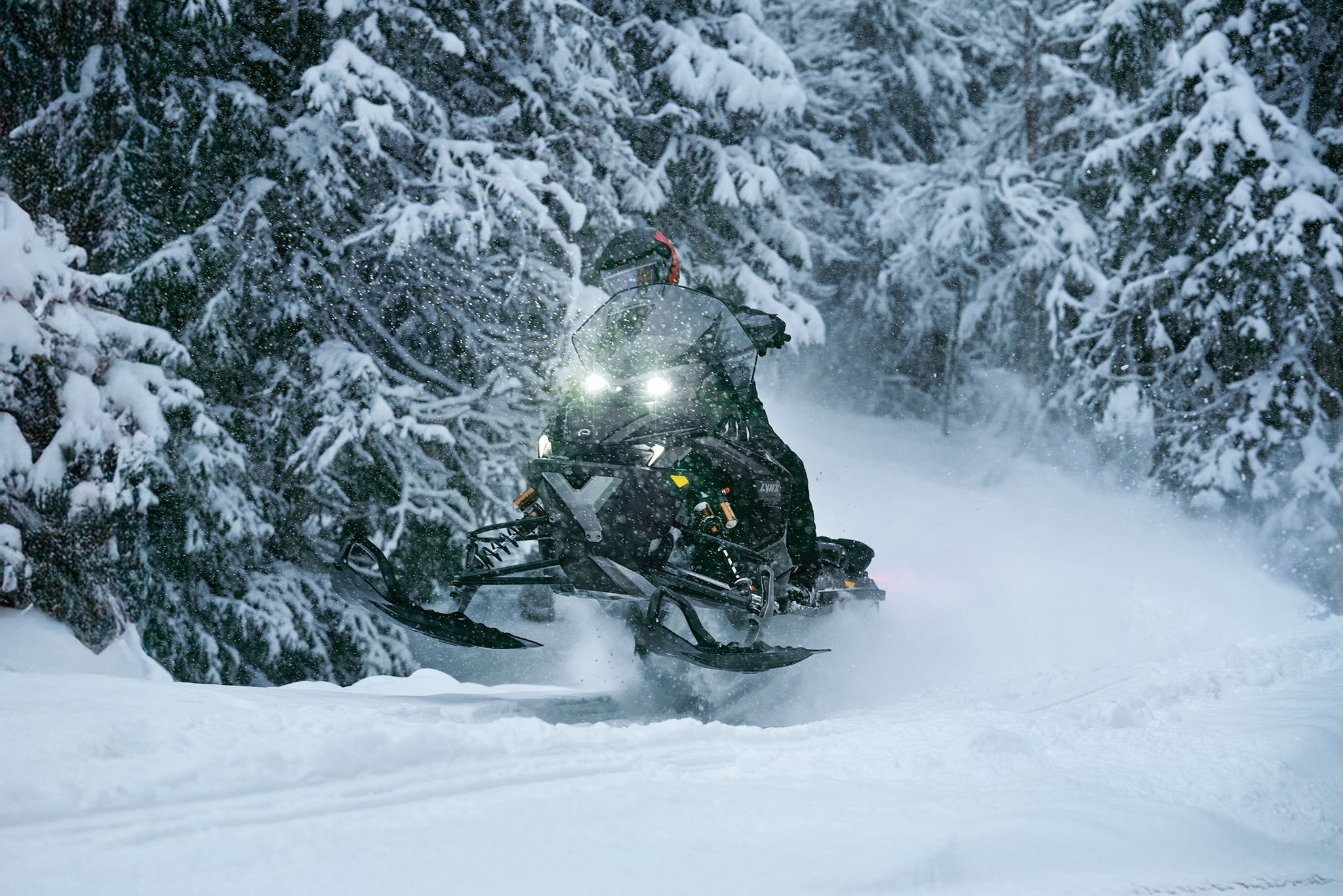 Förare kör en 2027 Lynx Xterrain snöskoter i hög hastighet i en snöig skog