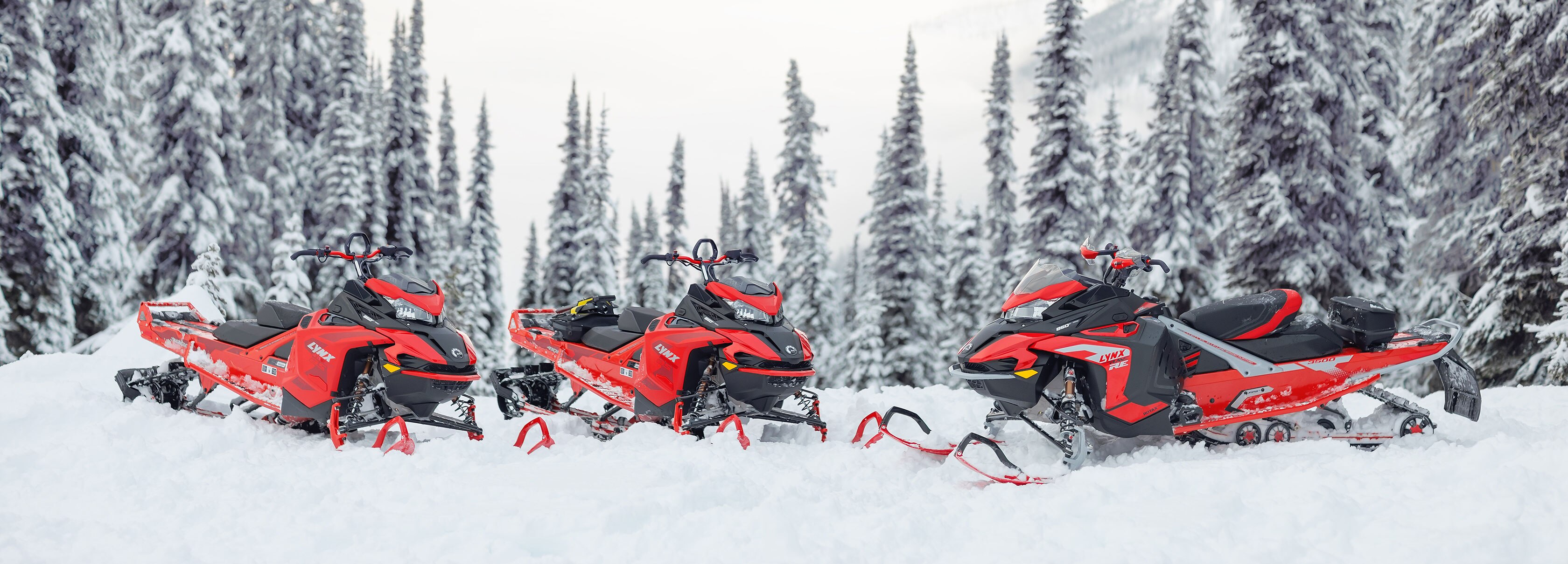 Tre Lynx-snøscootere i snødekt skog.