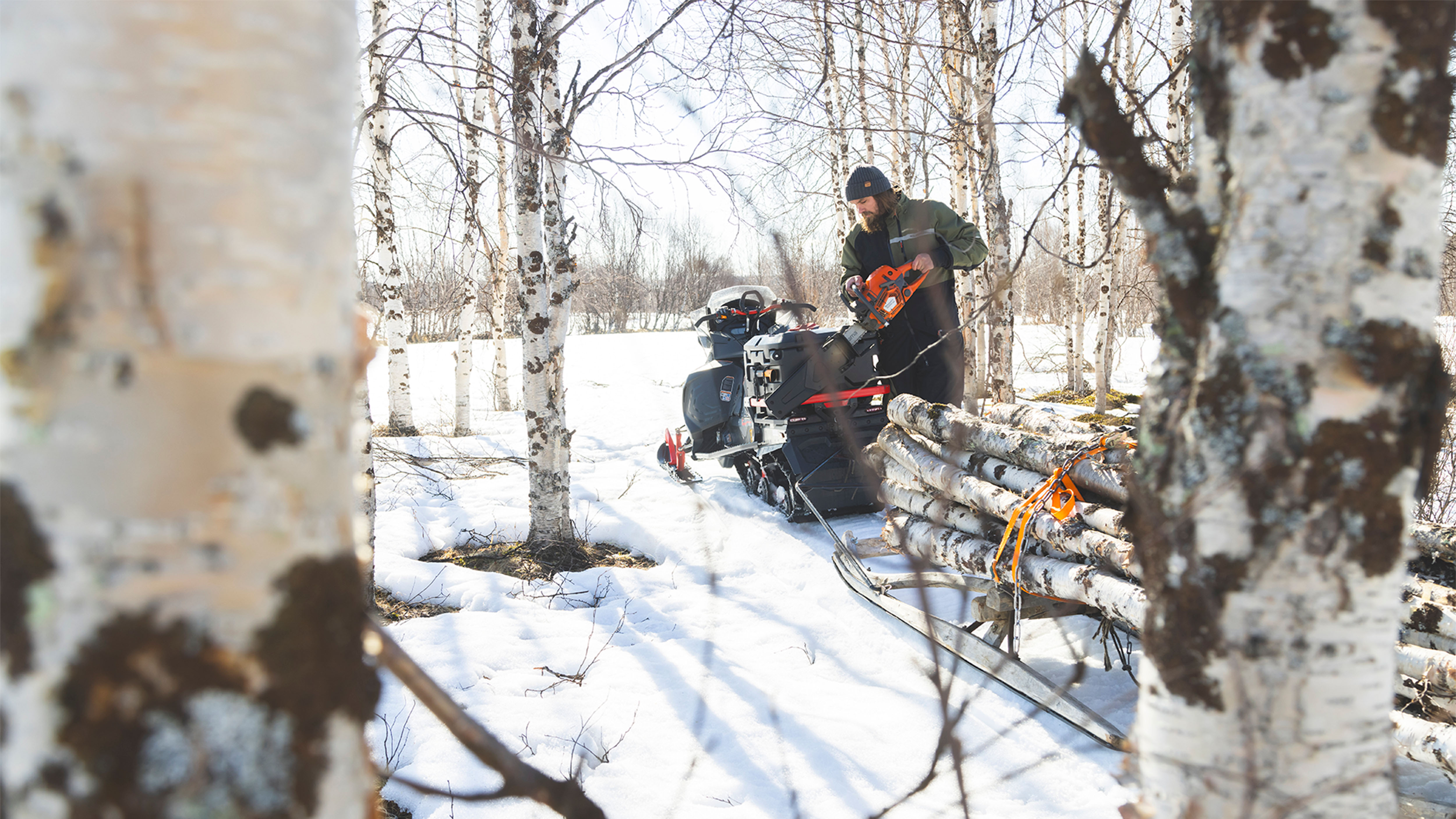 Man taking a chainsaw from the rear of the Lynx Commander Limited snowmobile 
