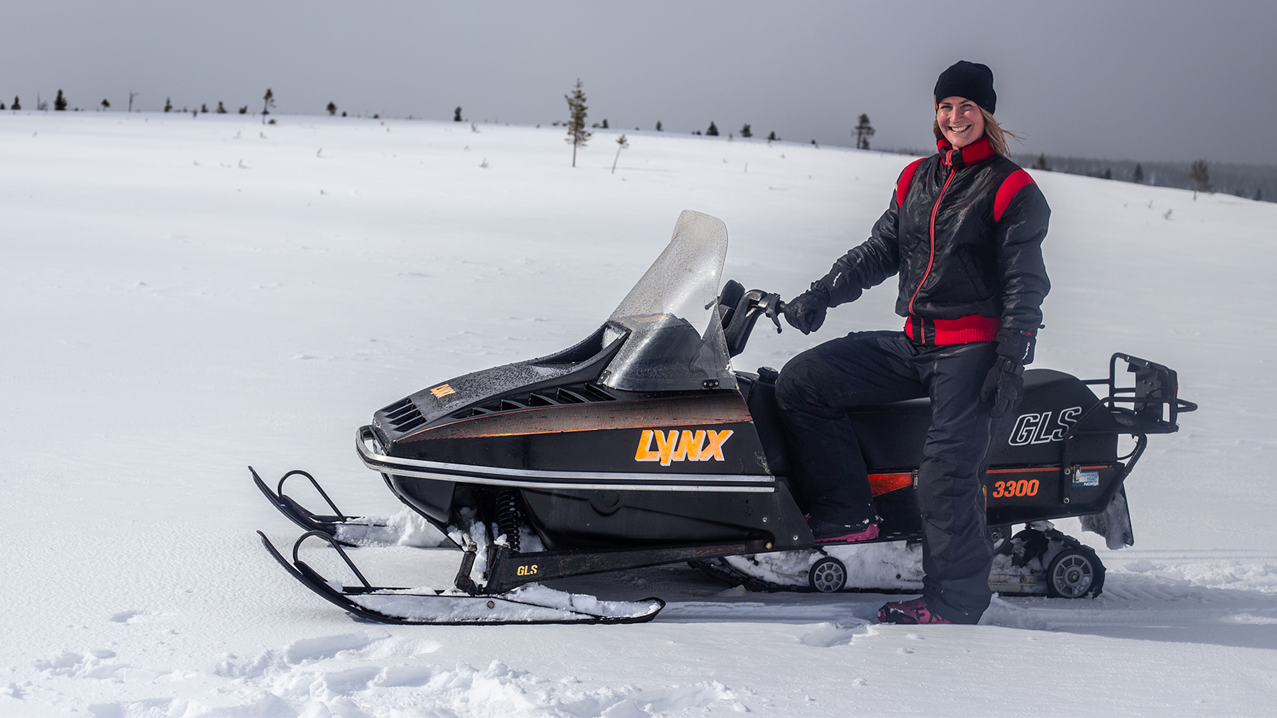 Woman smiling and standing next to Lynx GLS 3300 snowmobile on the fells