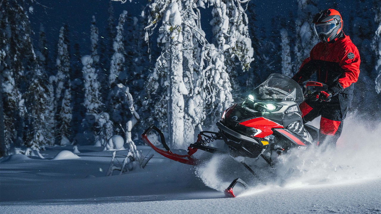 Motoneige Lynx Xterrain RE tournant sur la neige profonde dans une forêt sombre