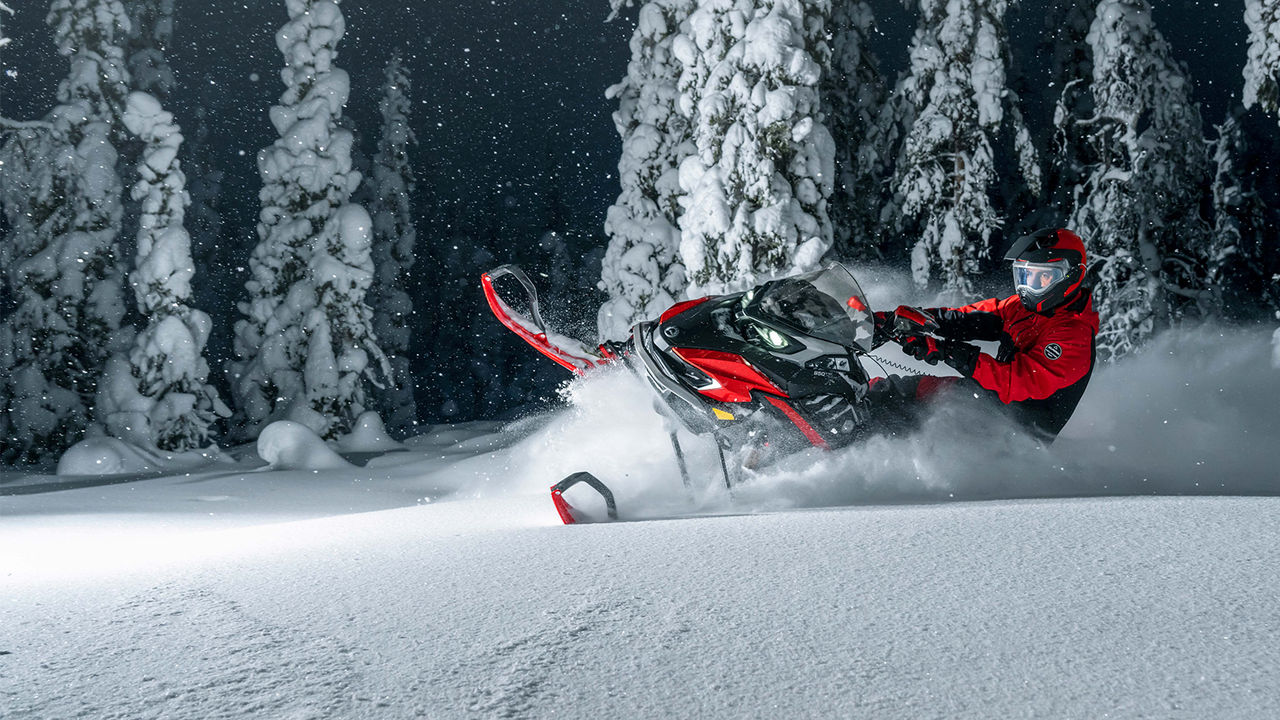 Lynx Xterrain RE snöskoter som svänger på djup snö i mörk skog