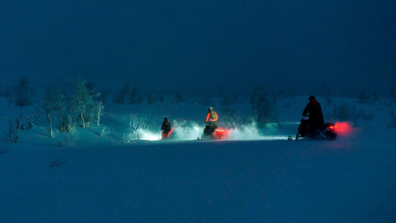 Tre Lynx snöskotrar i kö i mörkret