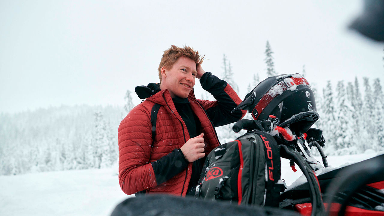 Rider having a break and laughing next to snowmobile