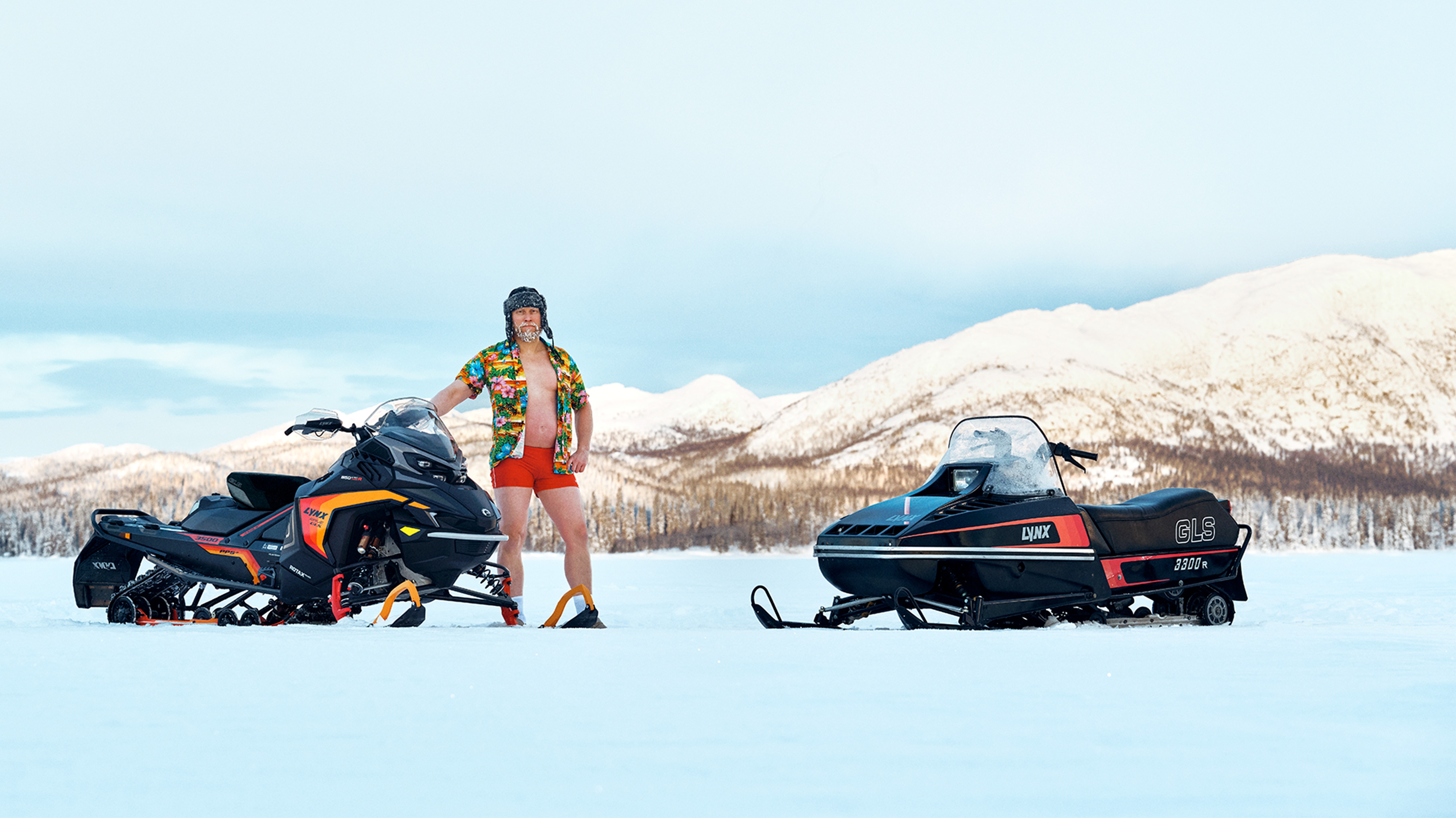 Man standing on lakeice with Lynx Rave GLS 2025 and retro GLS 3300 snowmobiles