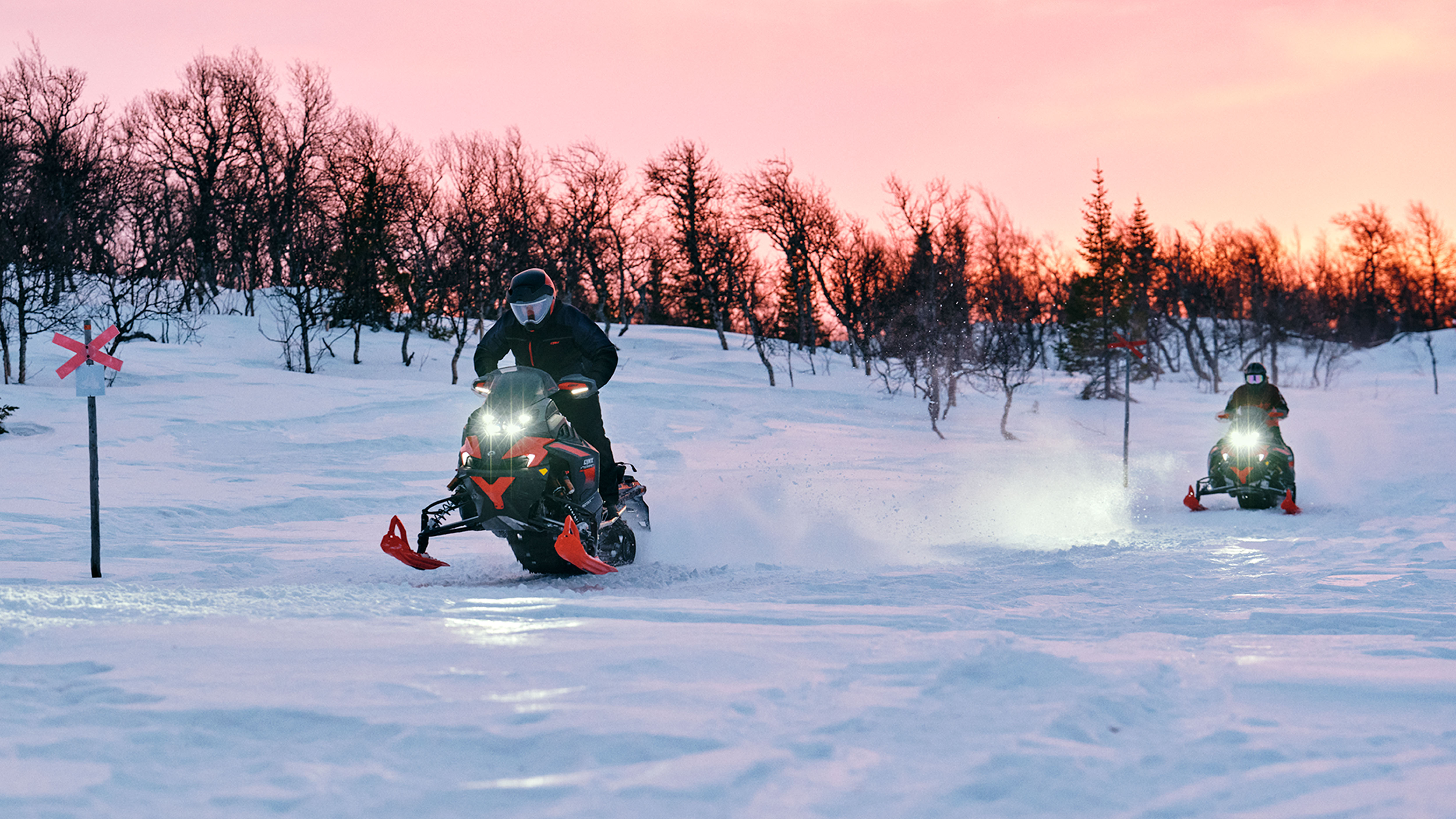 Kaksi Lynx Xterrain RE 2025 -moottorikelkkaa ajamassa reitillä auringonnousussa