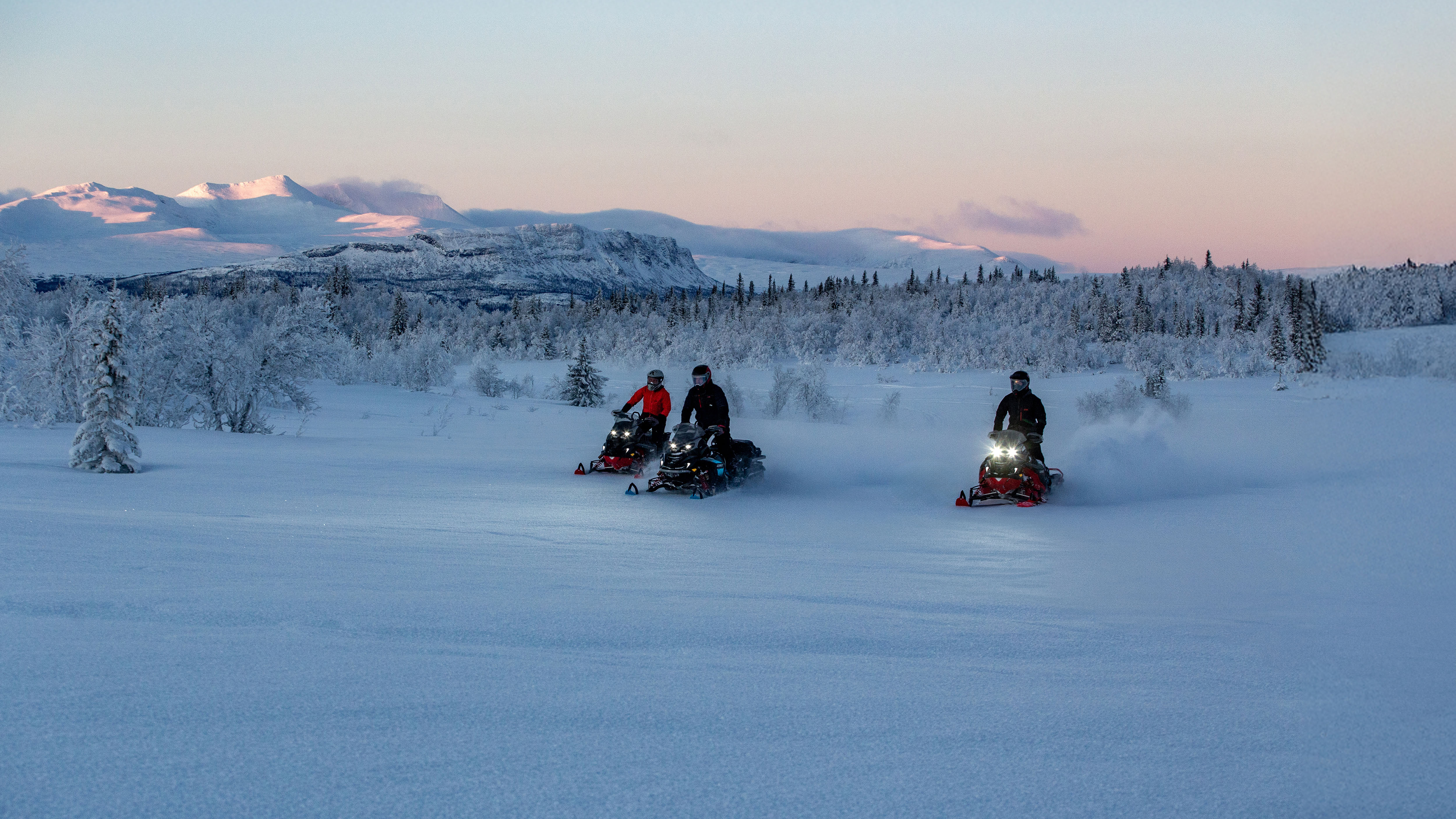 Three snowmobile riders riding on a snowy trail