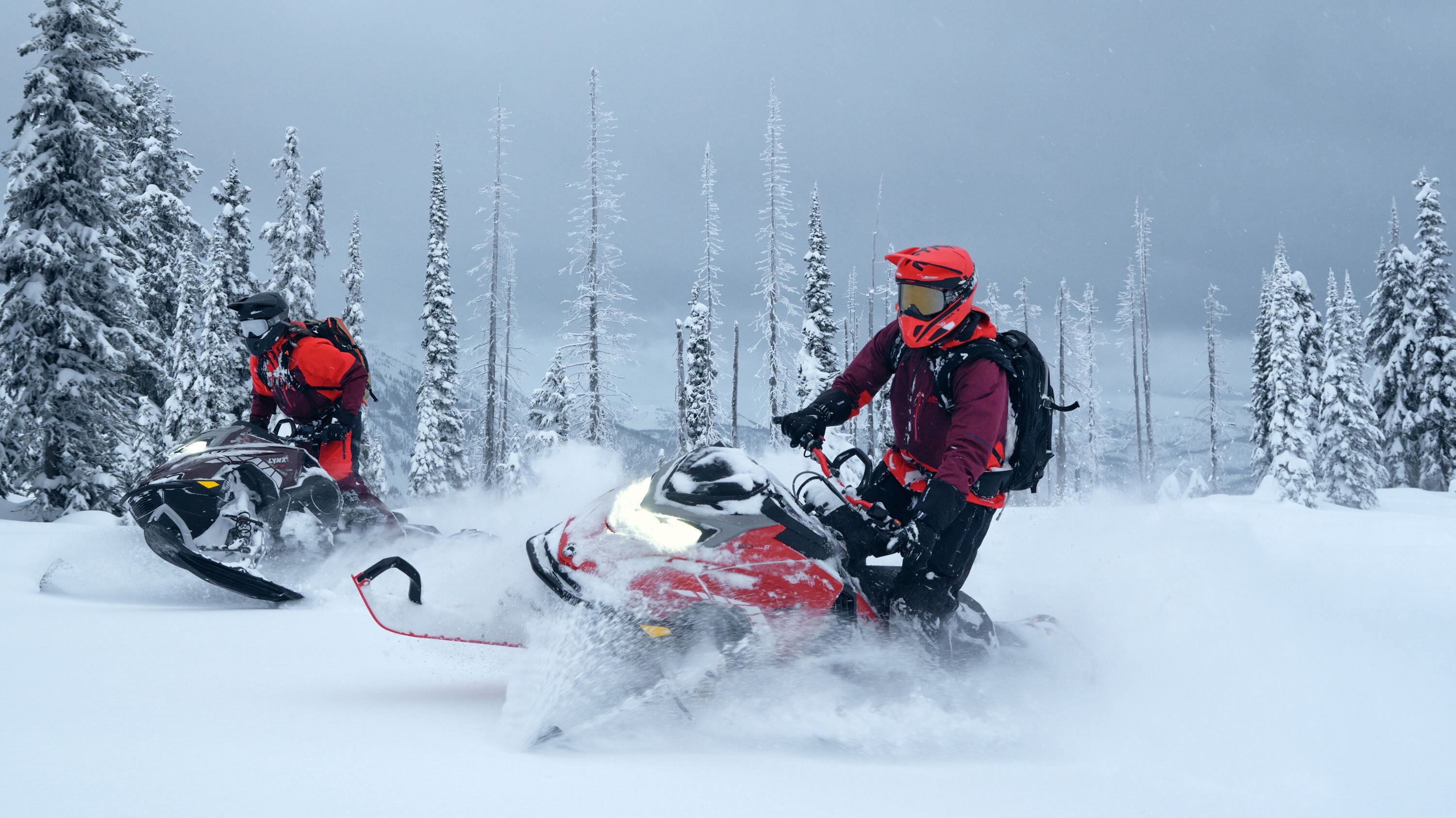 Två förare på sina Lynx Shredder-snöskotrar i djup snö