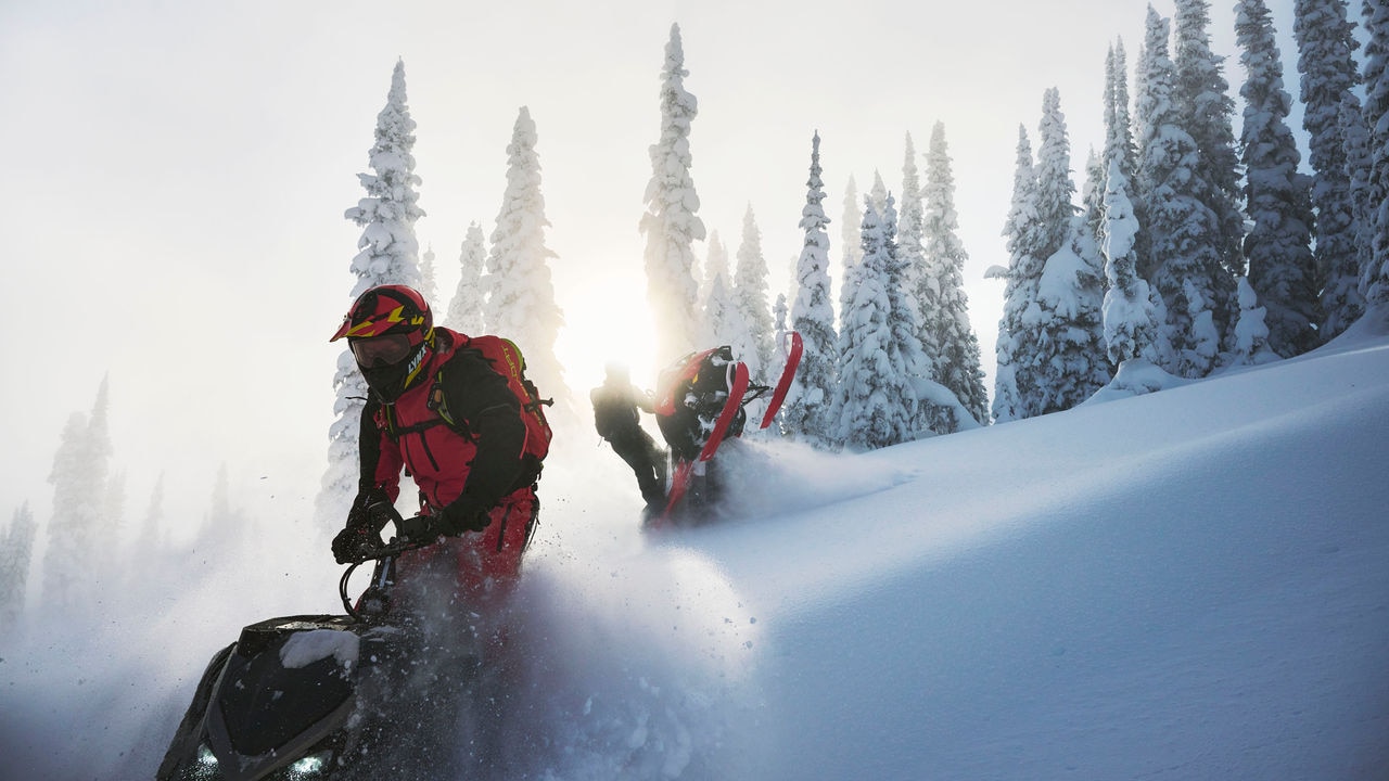 Three Lynx riders on their snowobile at the top of a mountain