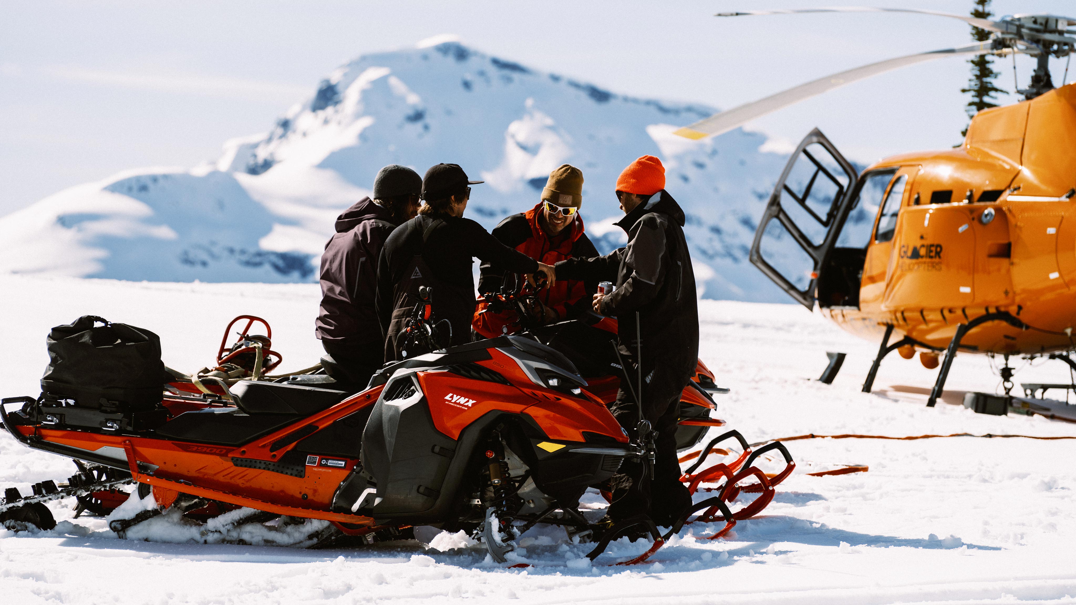 4 men gathering around Lynx snowmobiles in the mountain