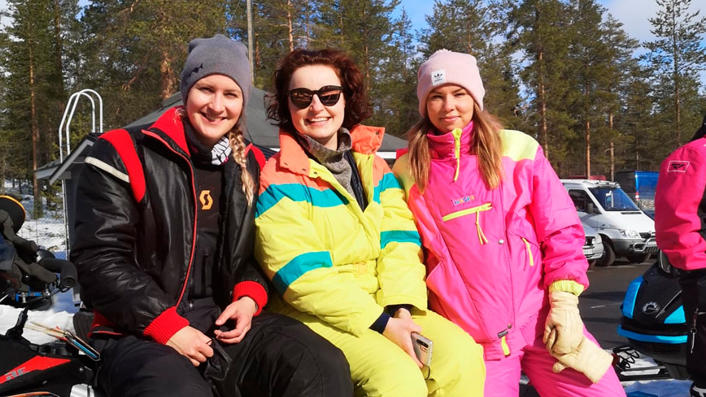 Three women sitting on vintage snowmobile with retro outfit