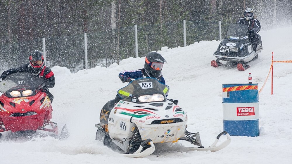 Vintage snowcross snowmobiles Lynx and Ski-Doo ride corner on a race track. 