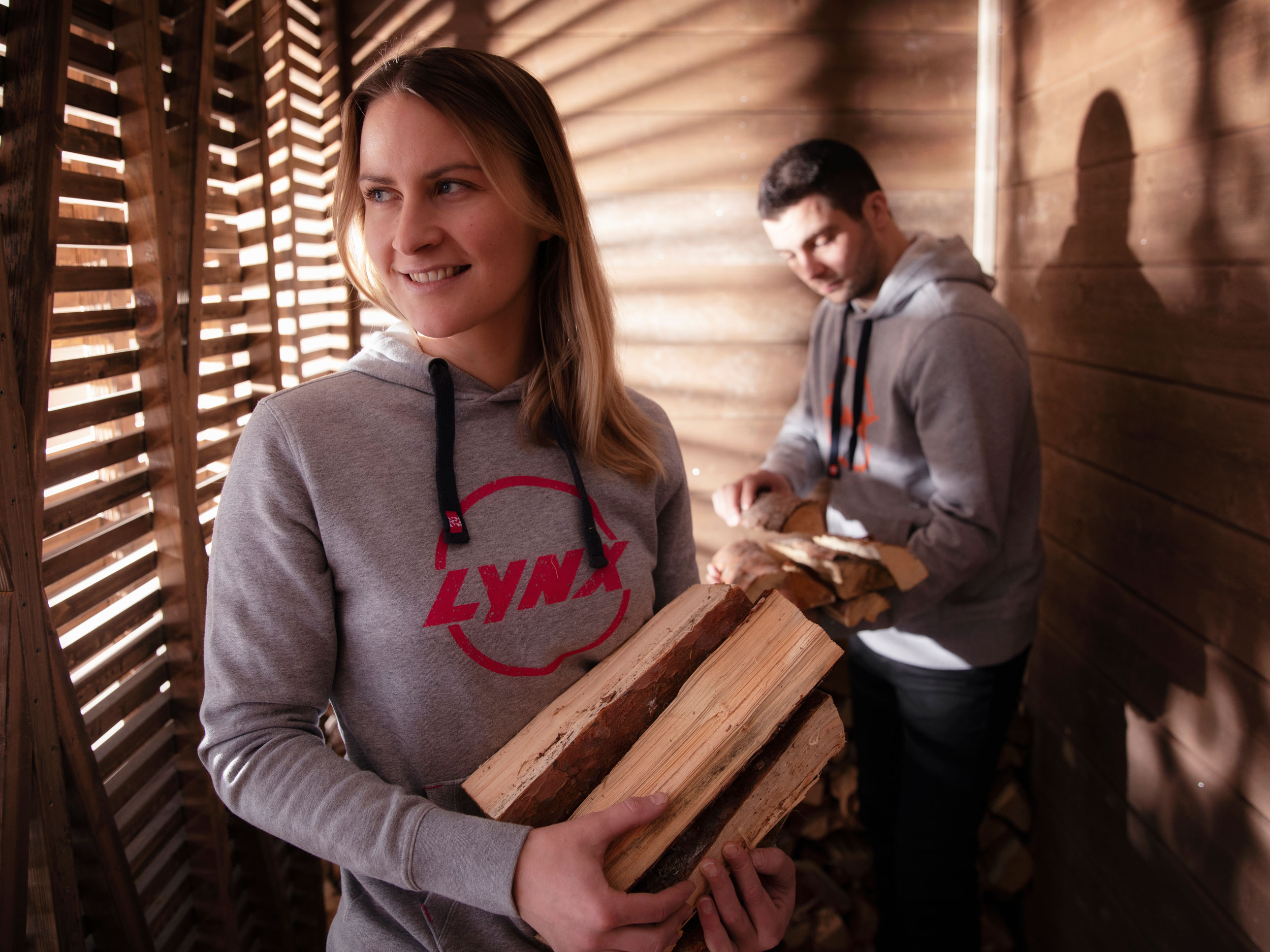 Man and woman wearing Lynx sportswear after riding and holding wood