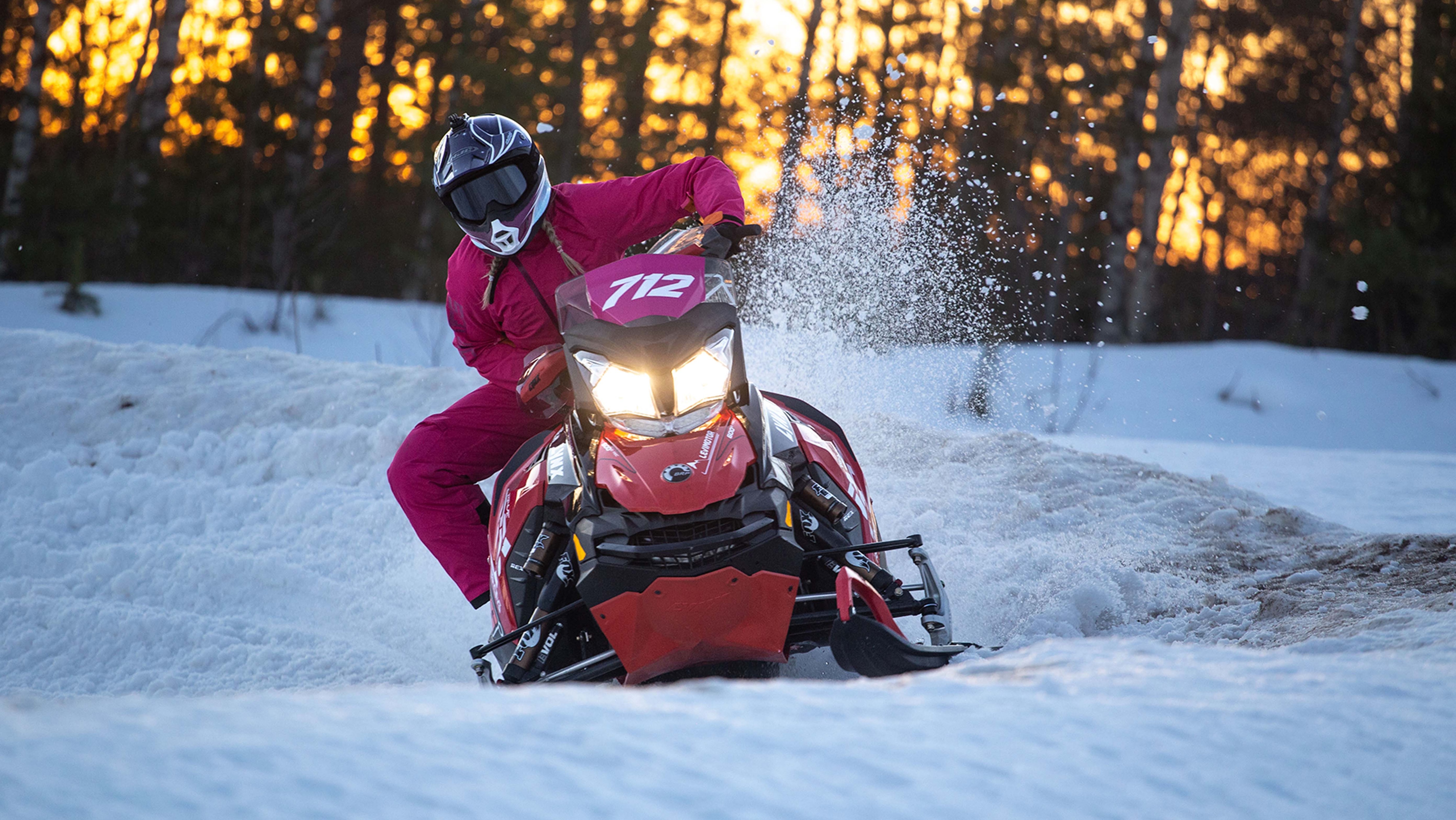 A woman rides a snowmobile in a corner at race track