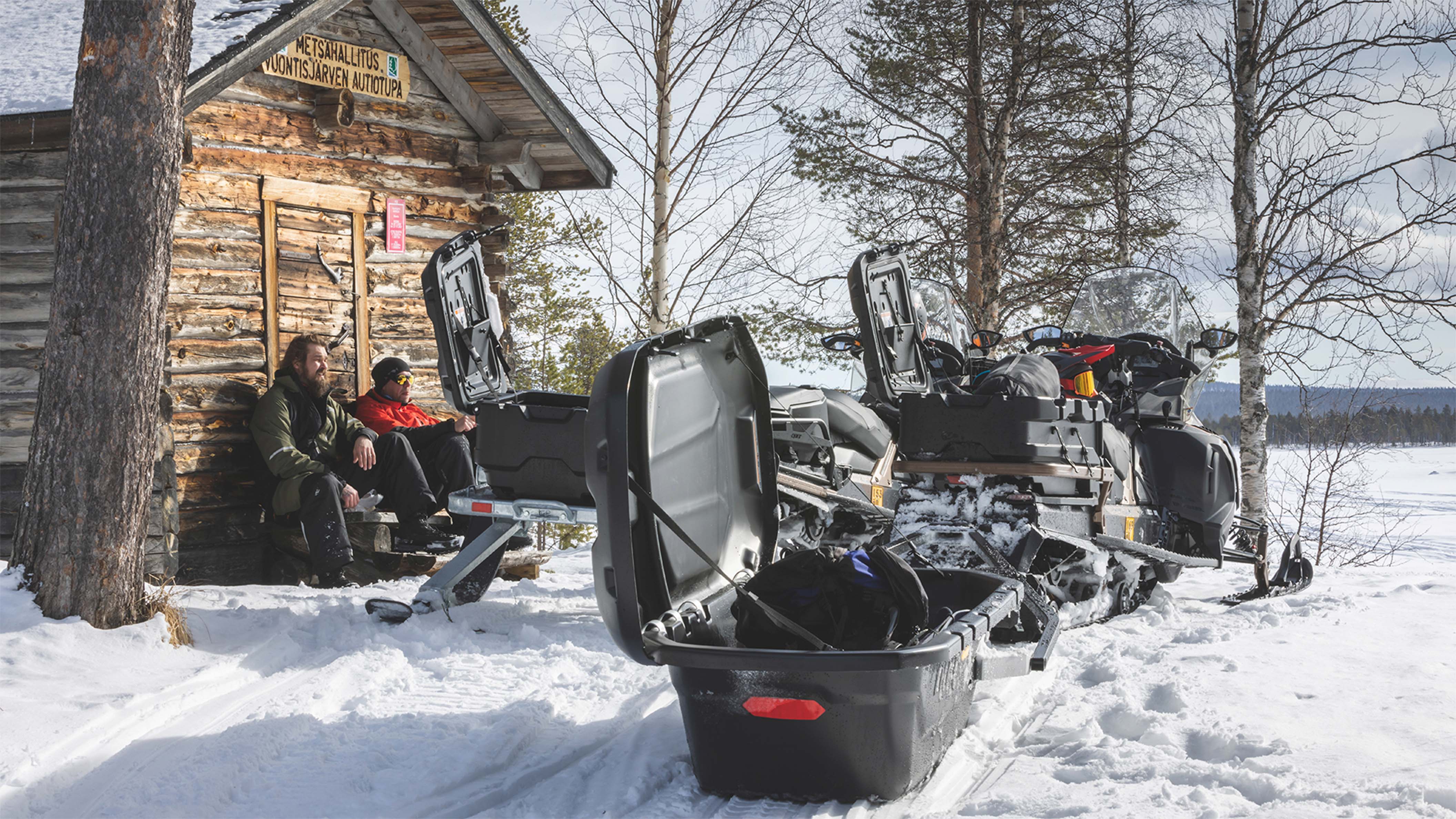 Two snowmobile riders are having a break at the wilderness hut