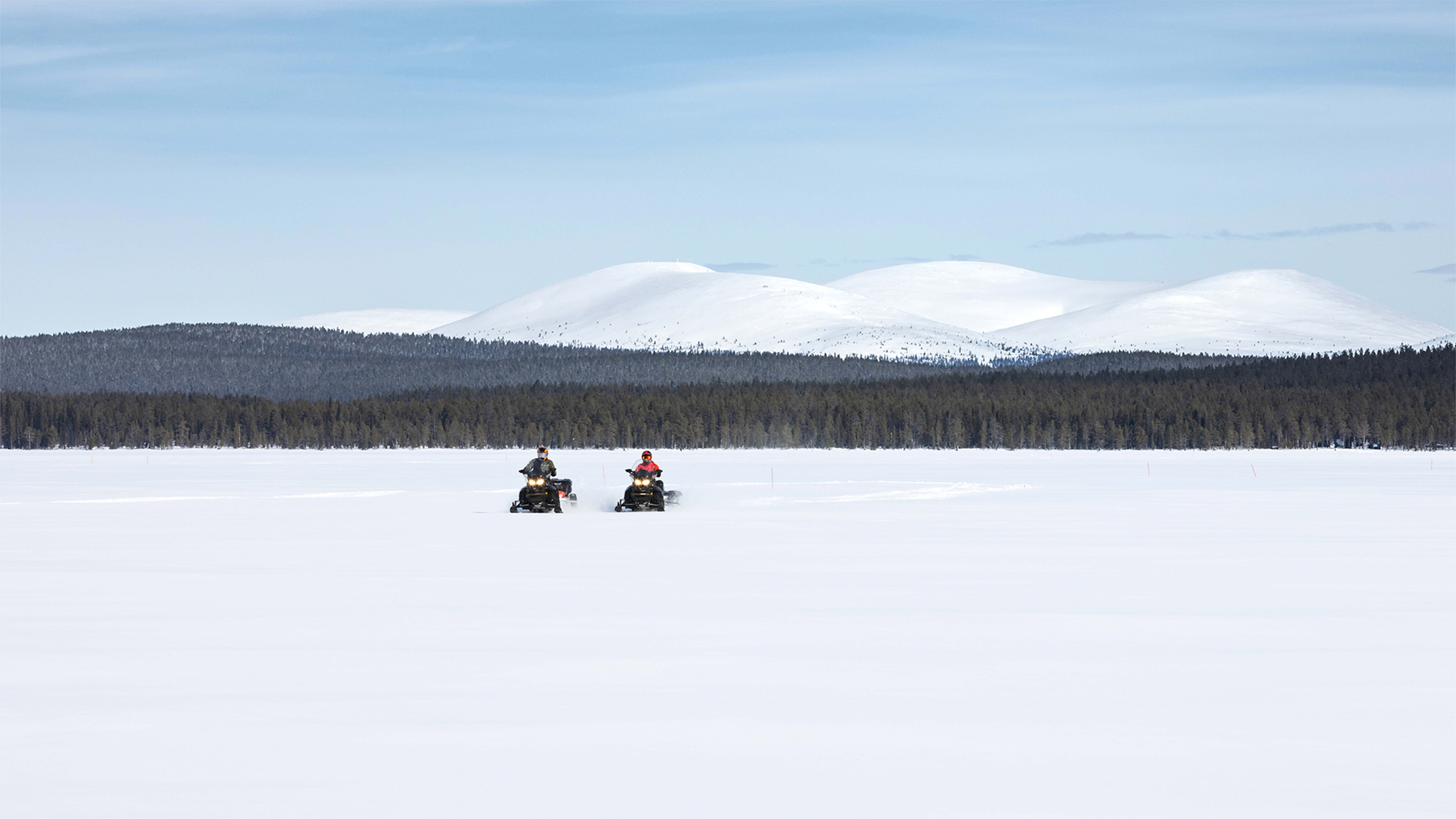 A Lynx 49 Ranger ST and Commander Grand Tourer snowmobiles respectively riding Finnish Lapland's lake