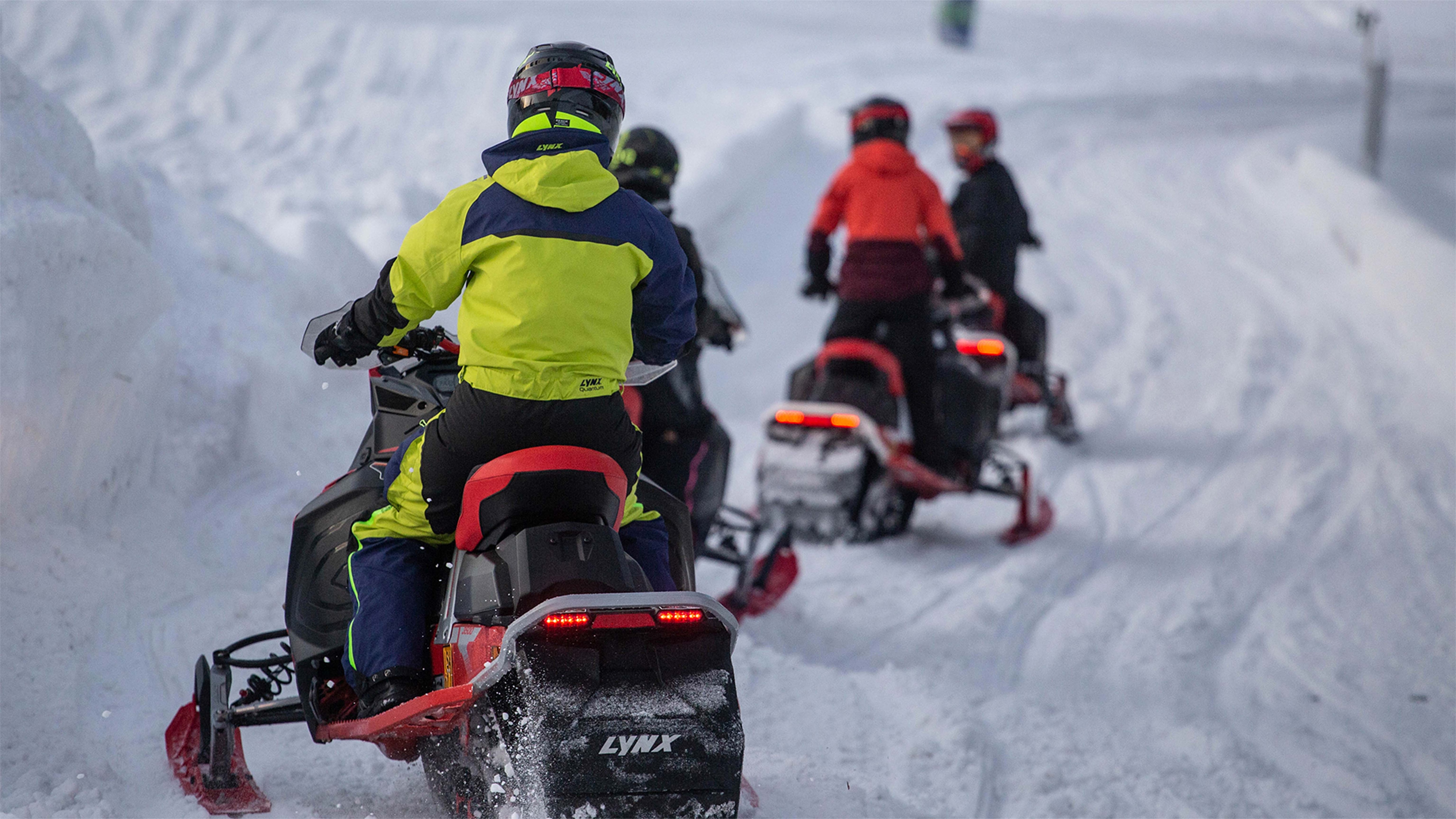 Four snowmobiles are riding on a trail in line