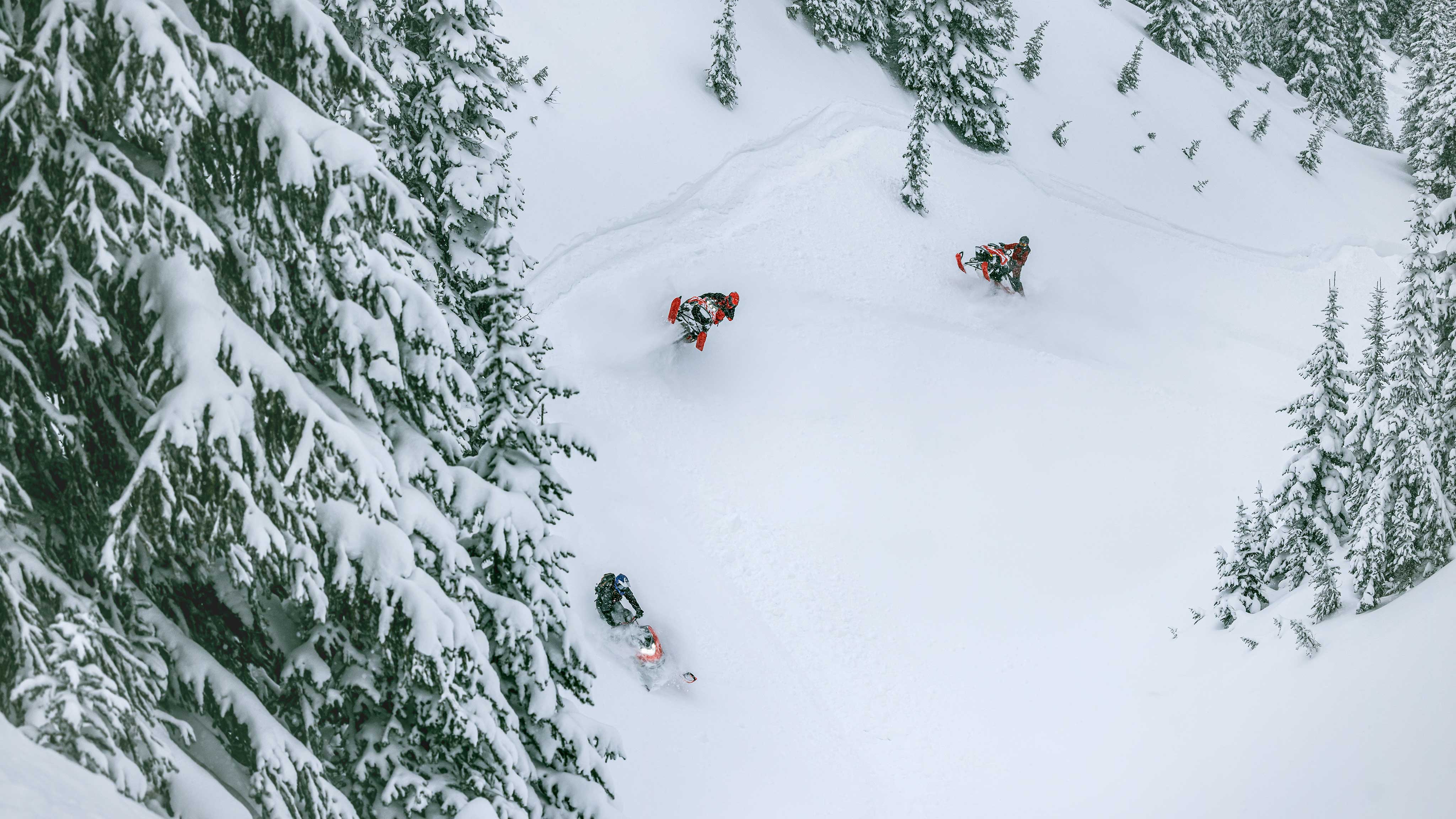 Tre Lynx-førere kjører snøscooter på et fjell.