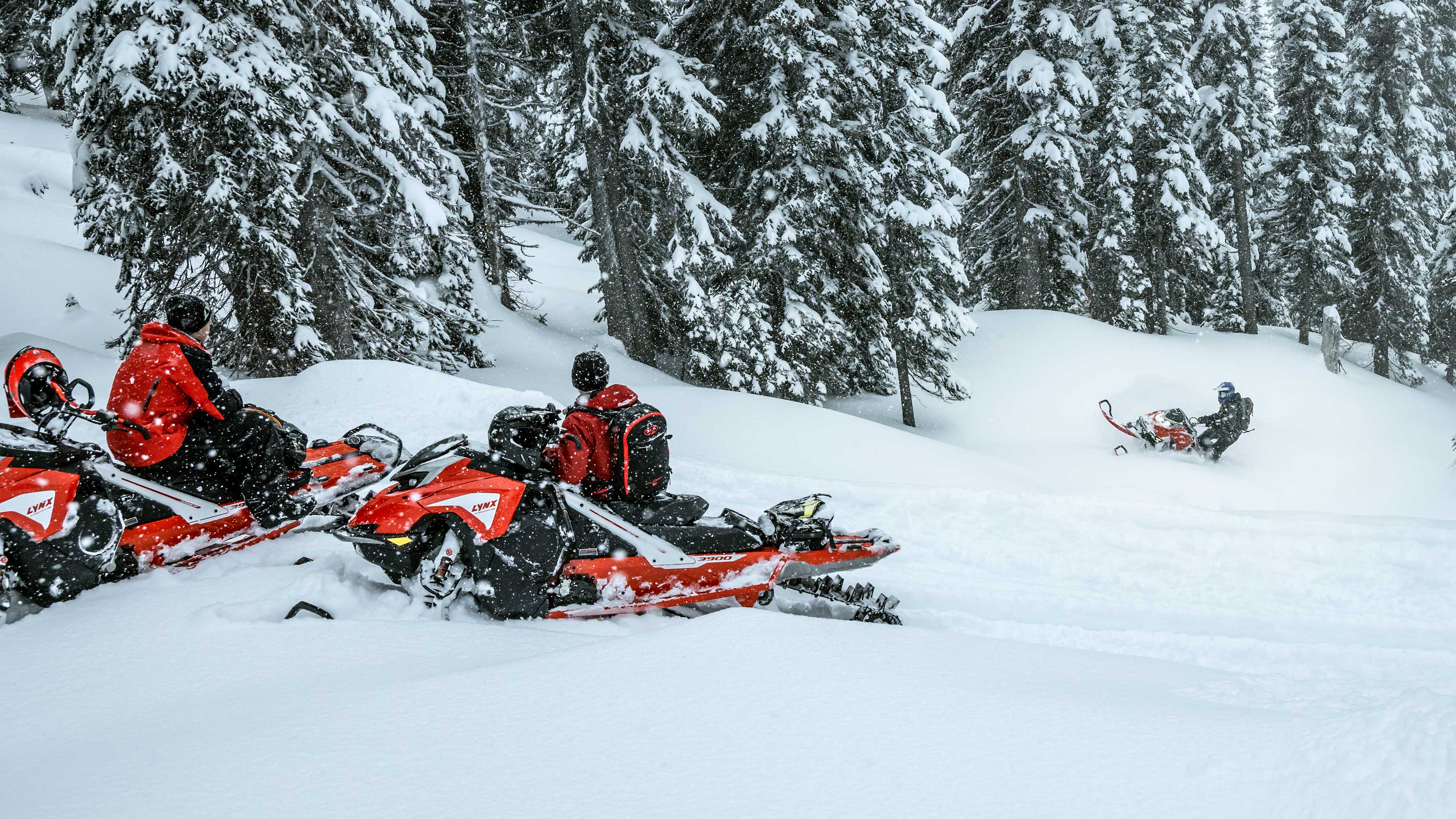 Two men are looking the third one who climbs the hill with deep snow snowmobile