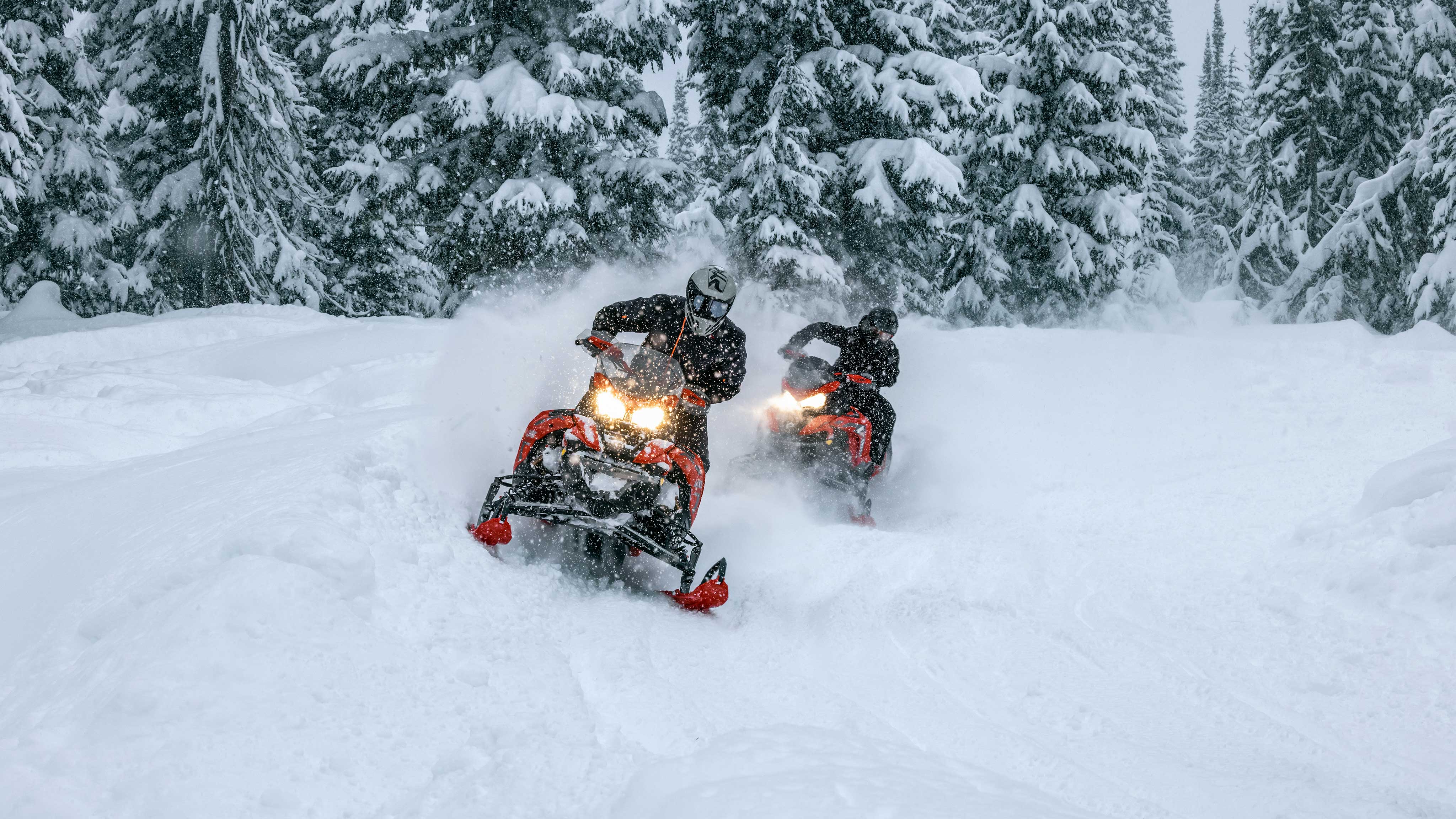 2 riders riding their Lynx snowmobile across a snowy field