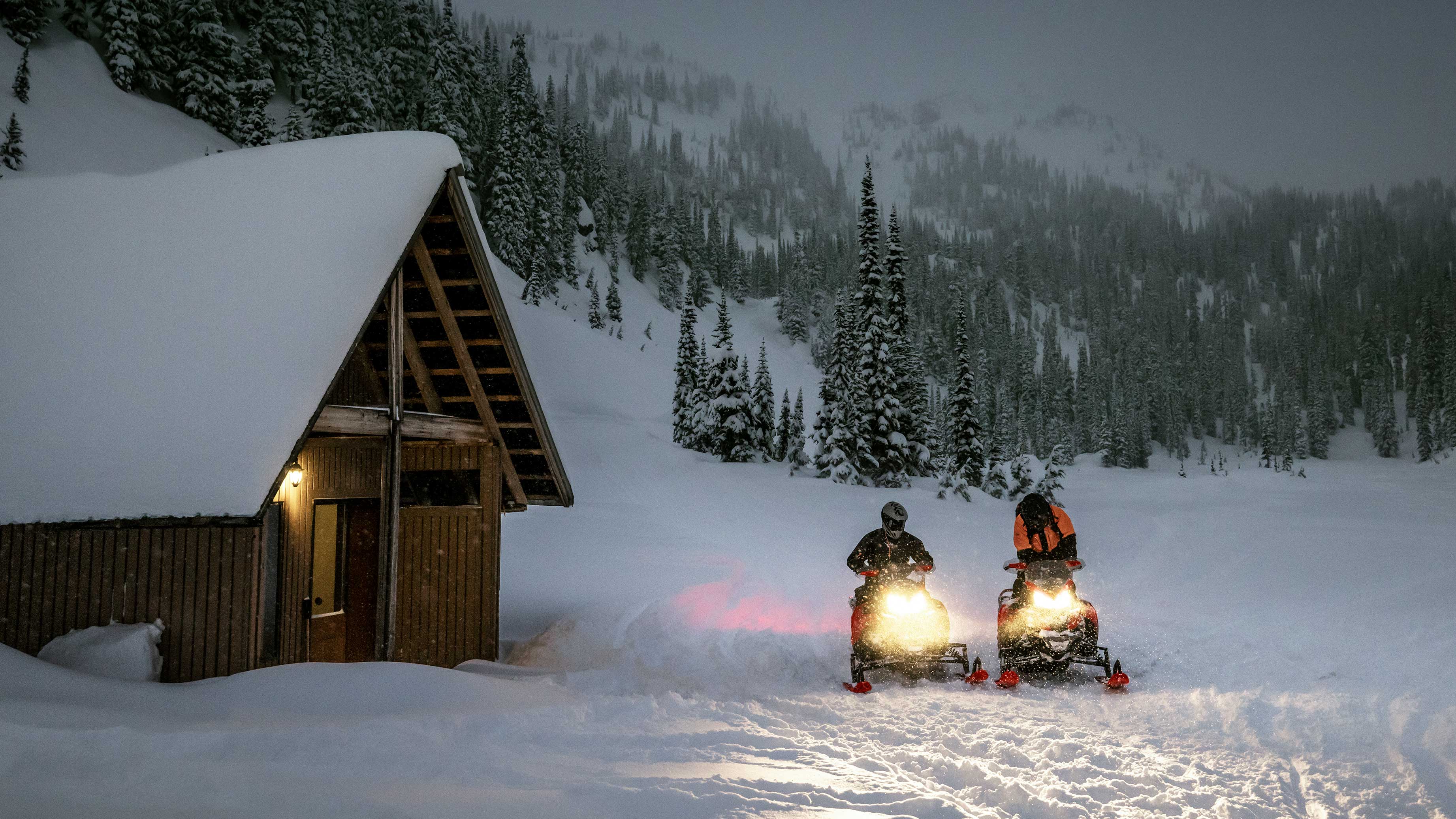 Two Lynx snowmobile riders arriving at a lodge