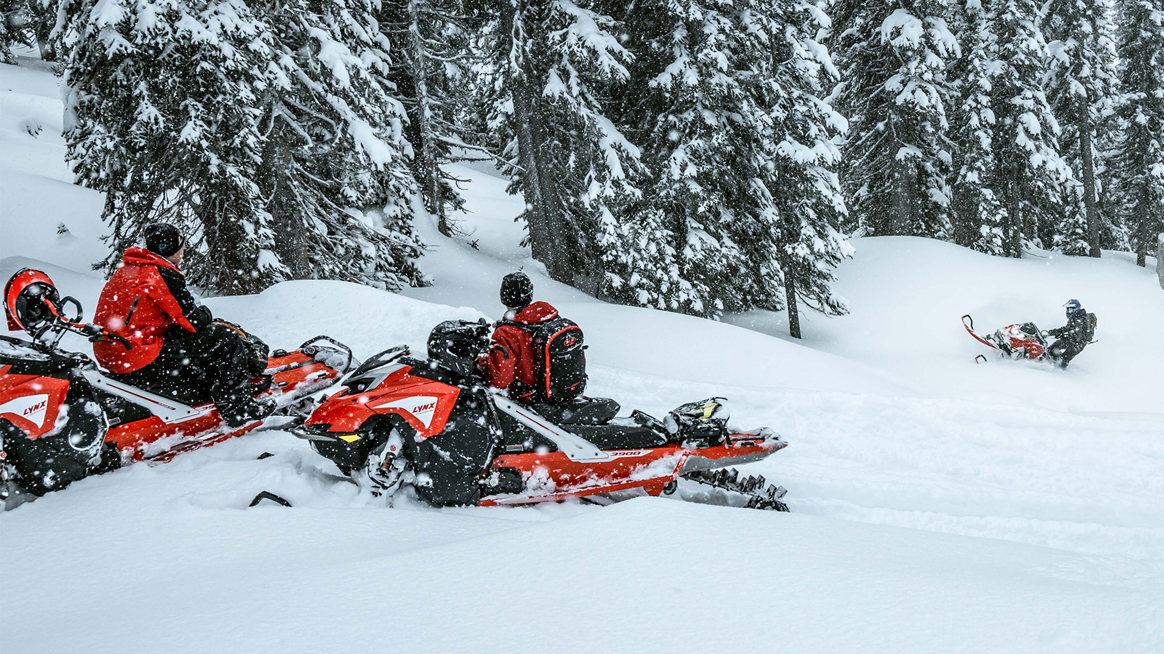 To menn ser på den tredje som klatrer opp bakken på sin dypsnøscooter