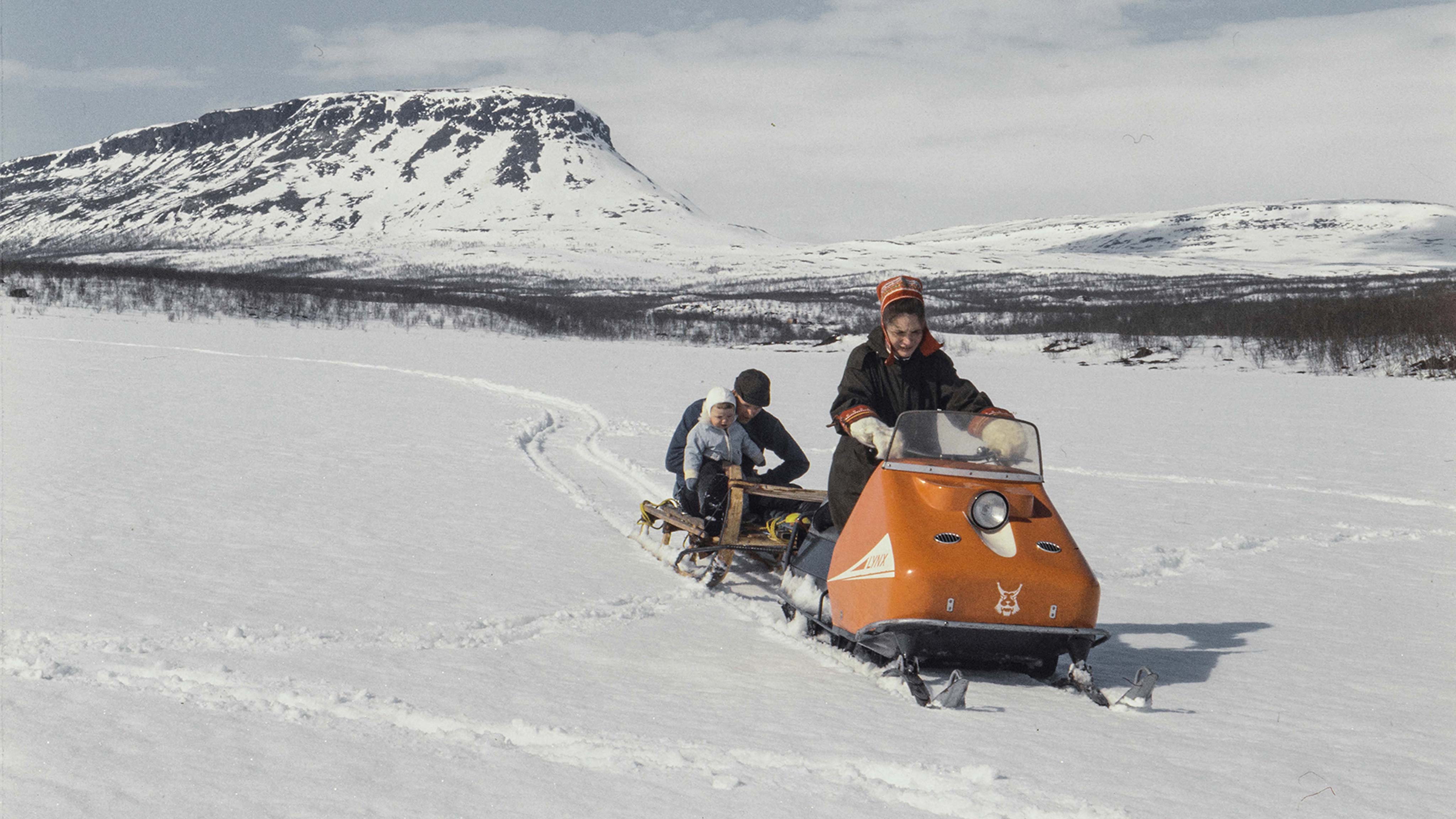  Nainen vetää reessä miestä ja lasta vuoden 1968 Lynx AS 50 moottorikelkalla Kilpisjärvellä