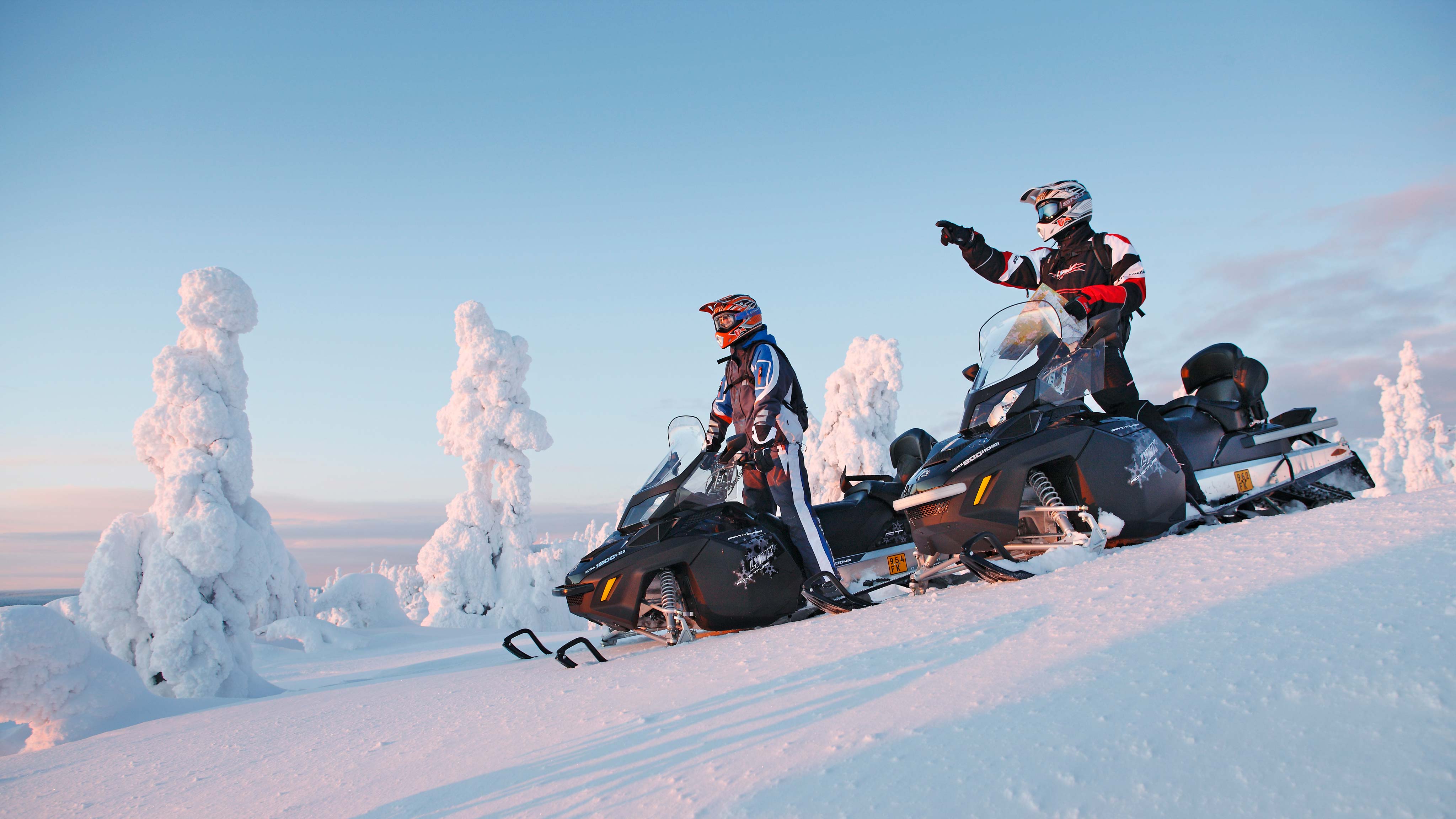 Menn som står på to Lynx Adventure Grand Tourer snøscootere og ser på naturen