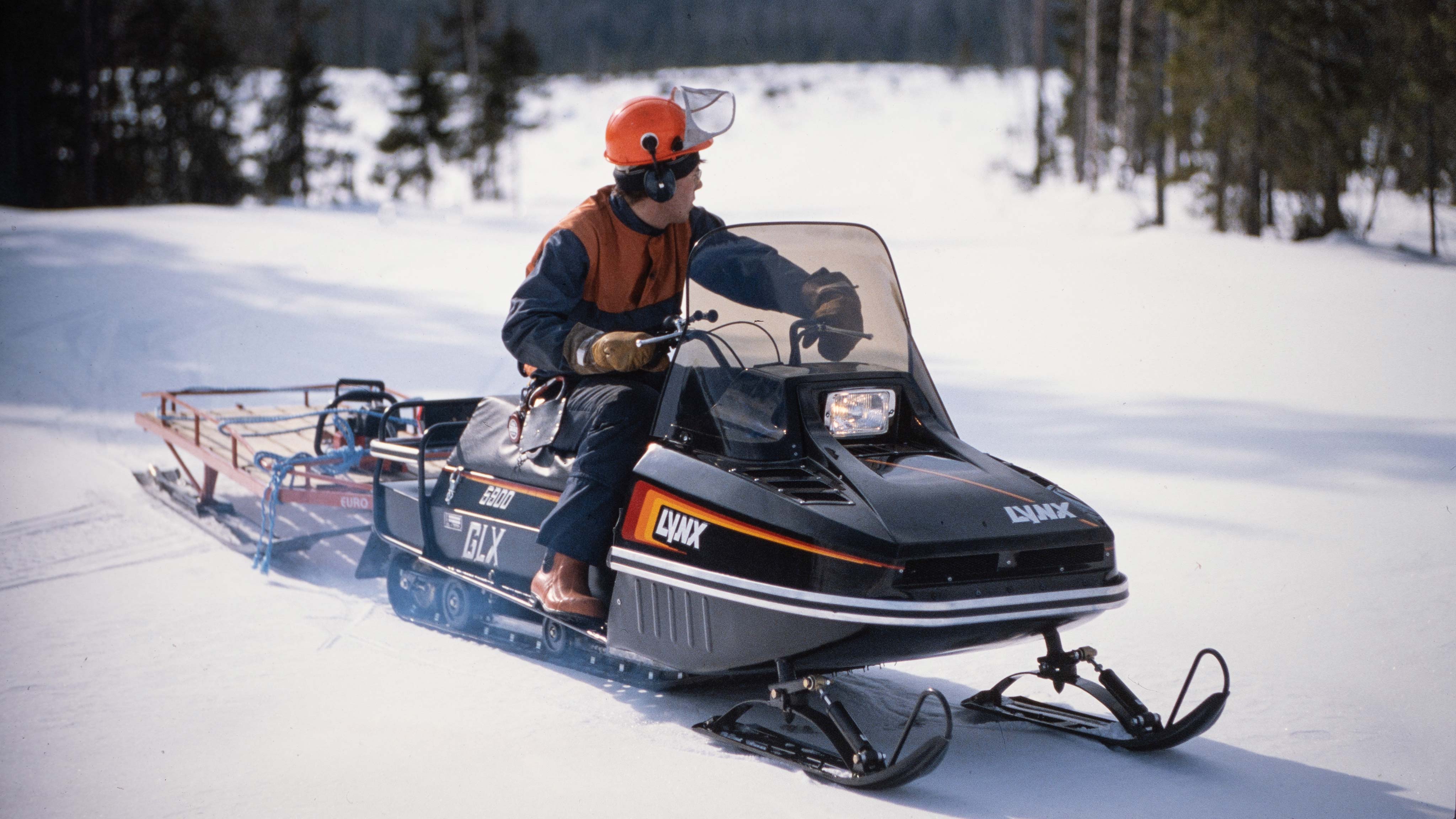 Man towing timber gear in s sleigh with Lynx GLX 5900 1986 snowmobile