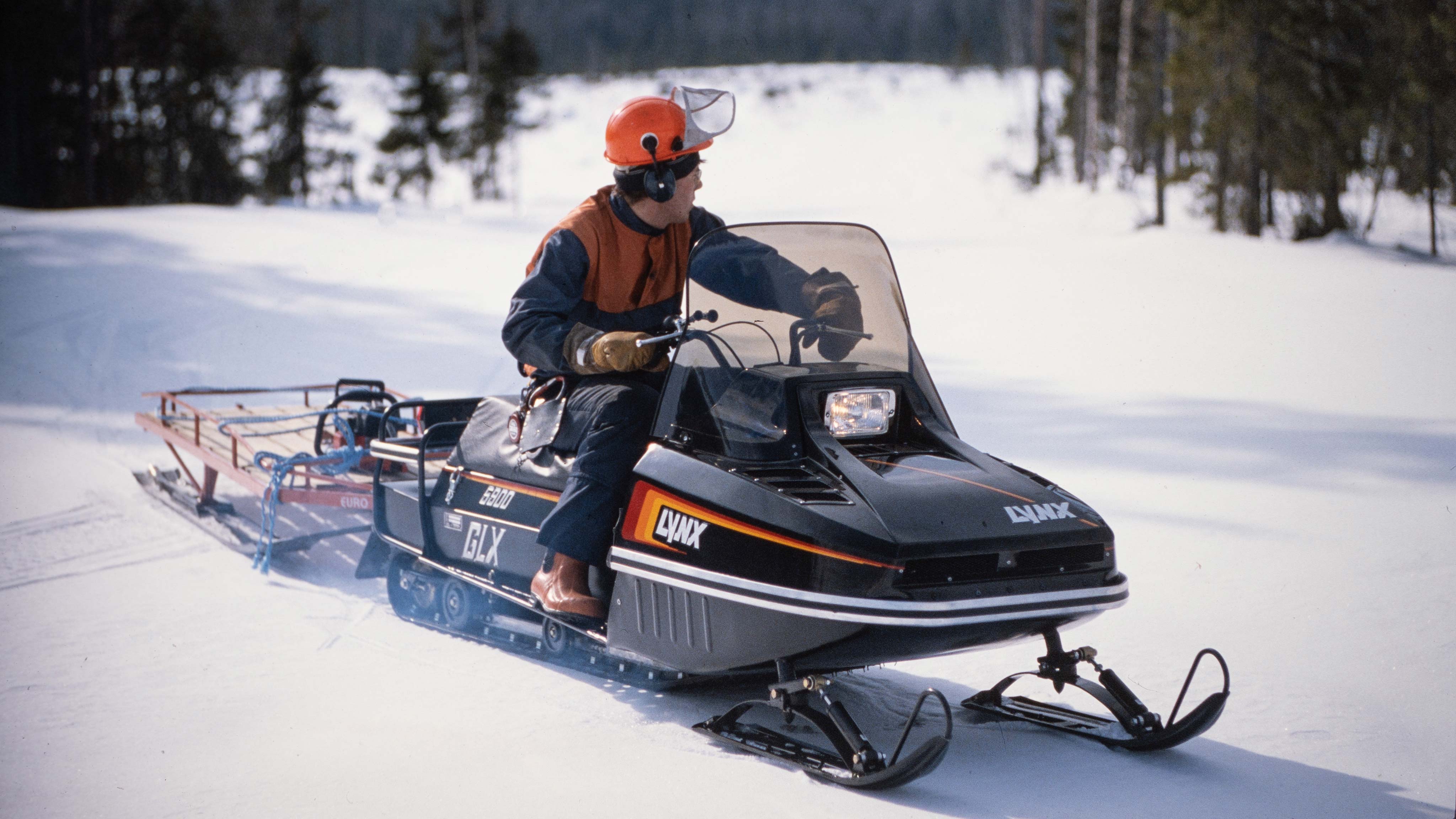 Mann sleper tømmerutstyr i slede med Lynx GLX 5900 1986 snøscooter