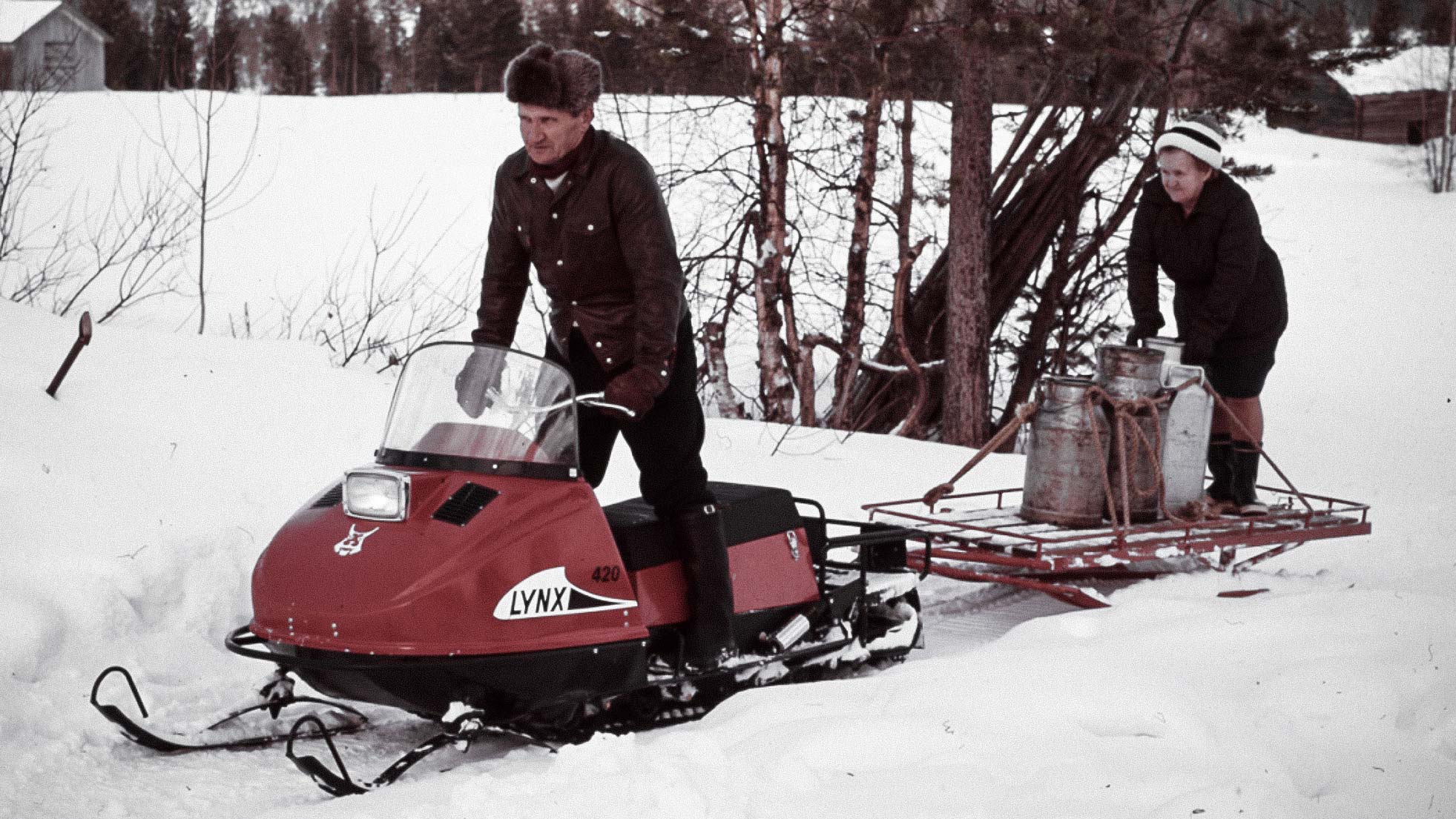 Couple towing a sleigh with Lynx 420 1974 snowmobile