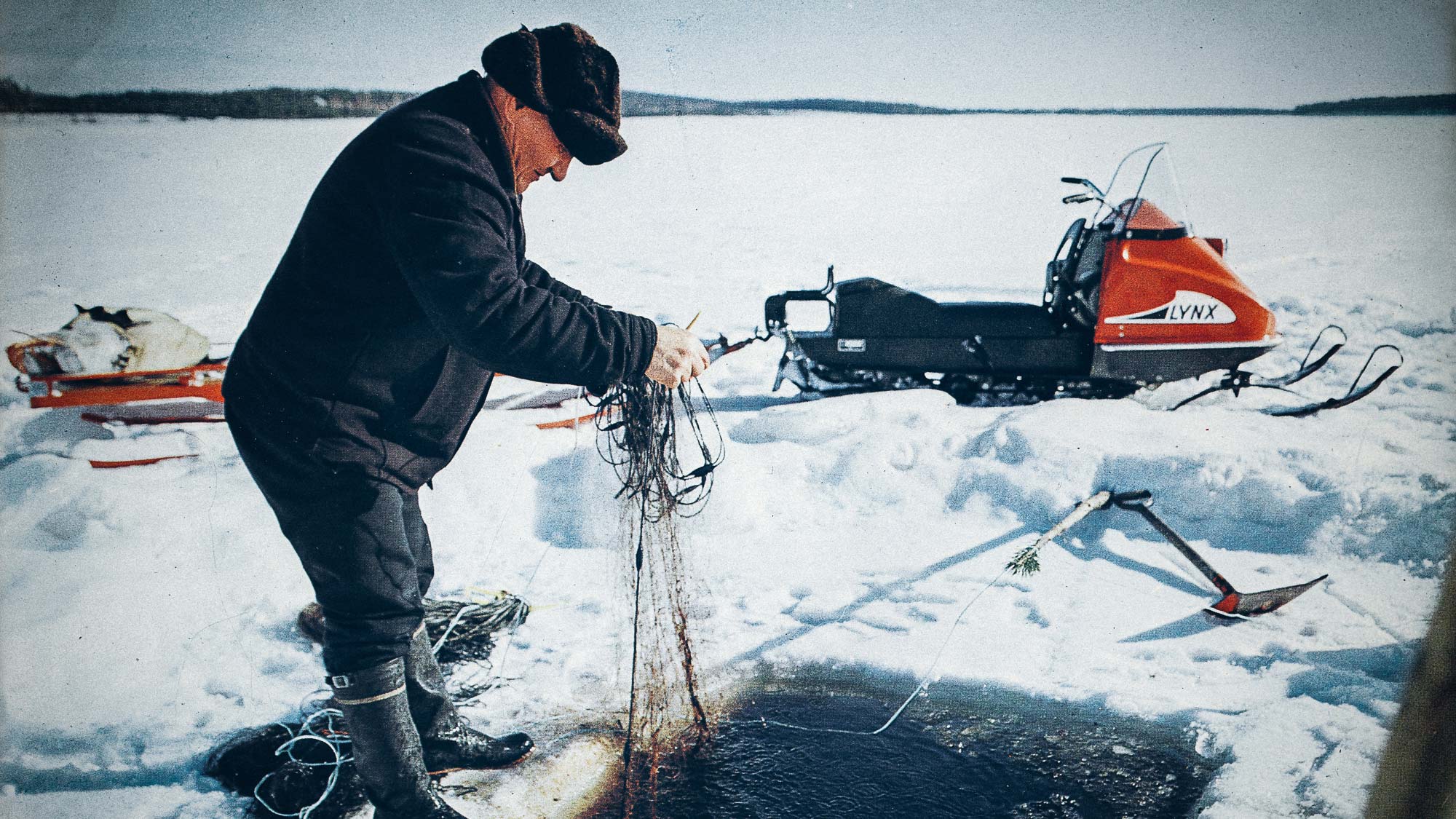 Un homme manipulant des filets de pêche sur la glace avec une motoneige Lynx 400 des années 1970