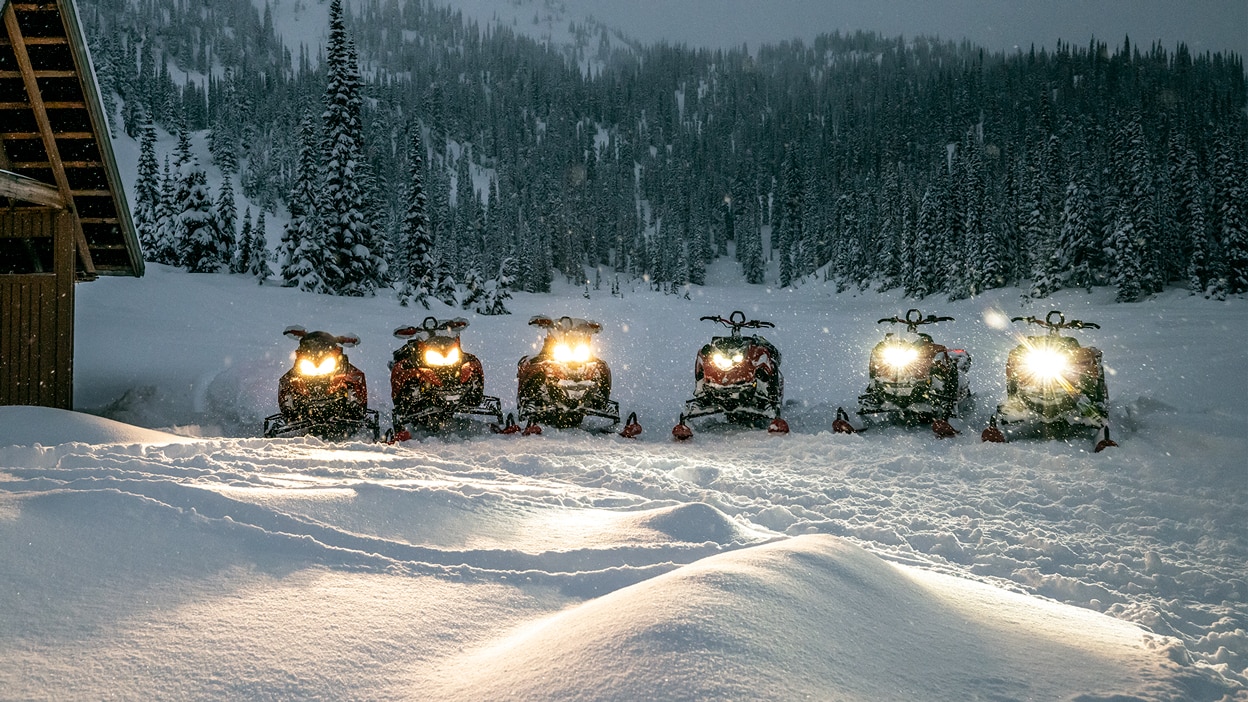 Six Lynx snowmobiles parked front of the cabin