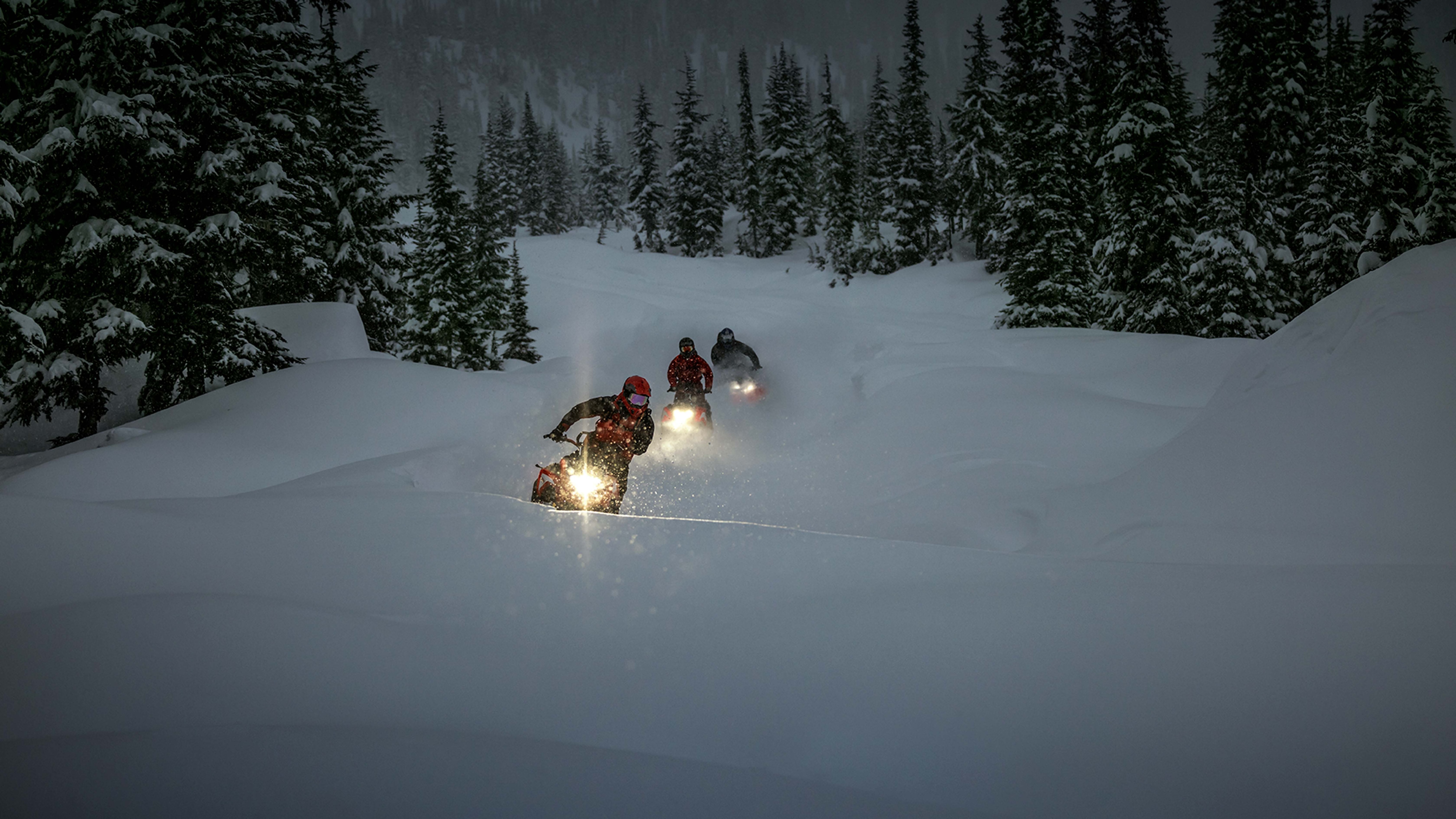 three Lynx Shredders snowmobiles riding in dark forest