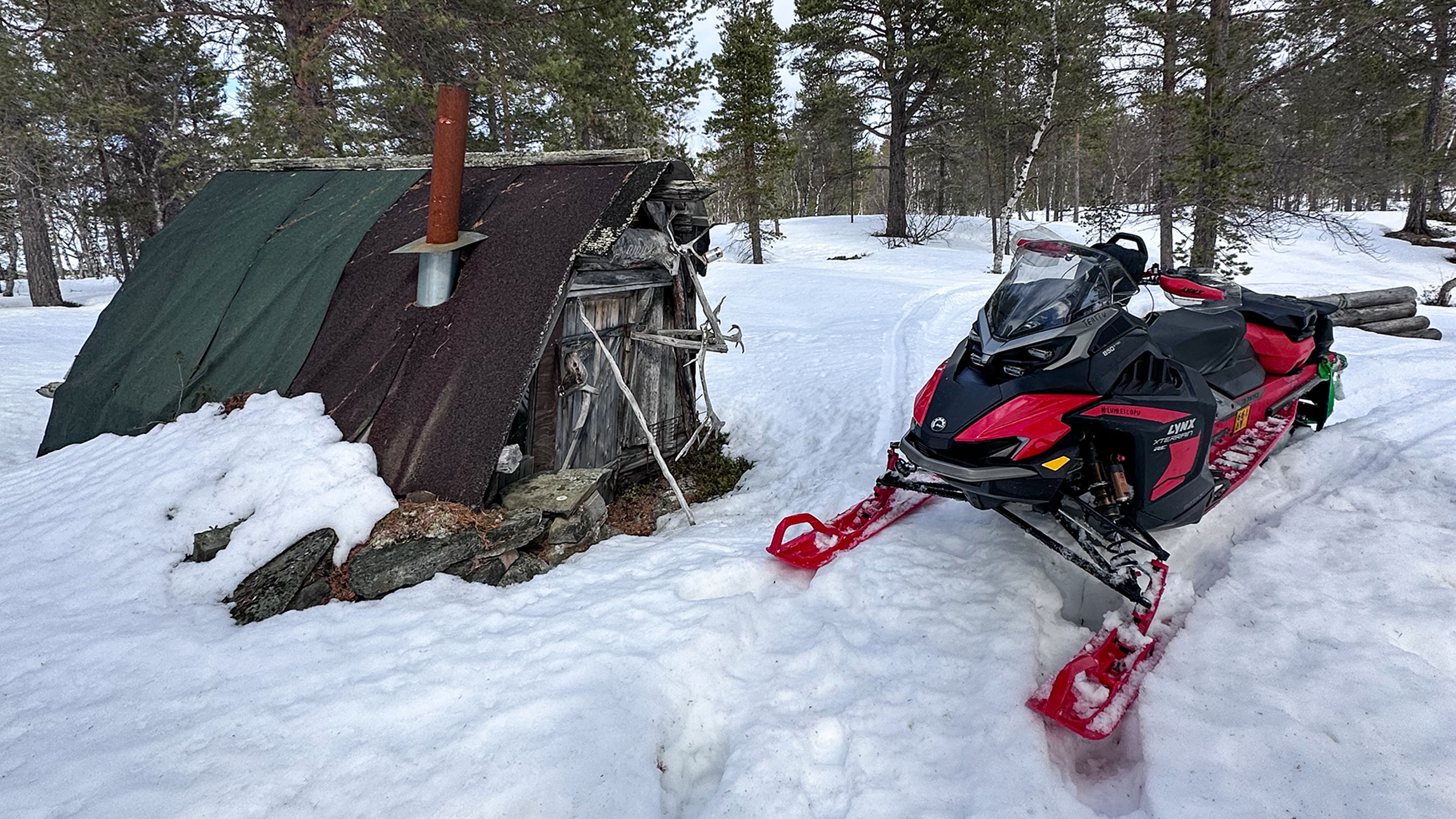Lynx Xterrain RE 850 E-TEC crossover snowmobile parked next to an old wilderness hut