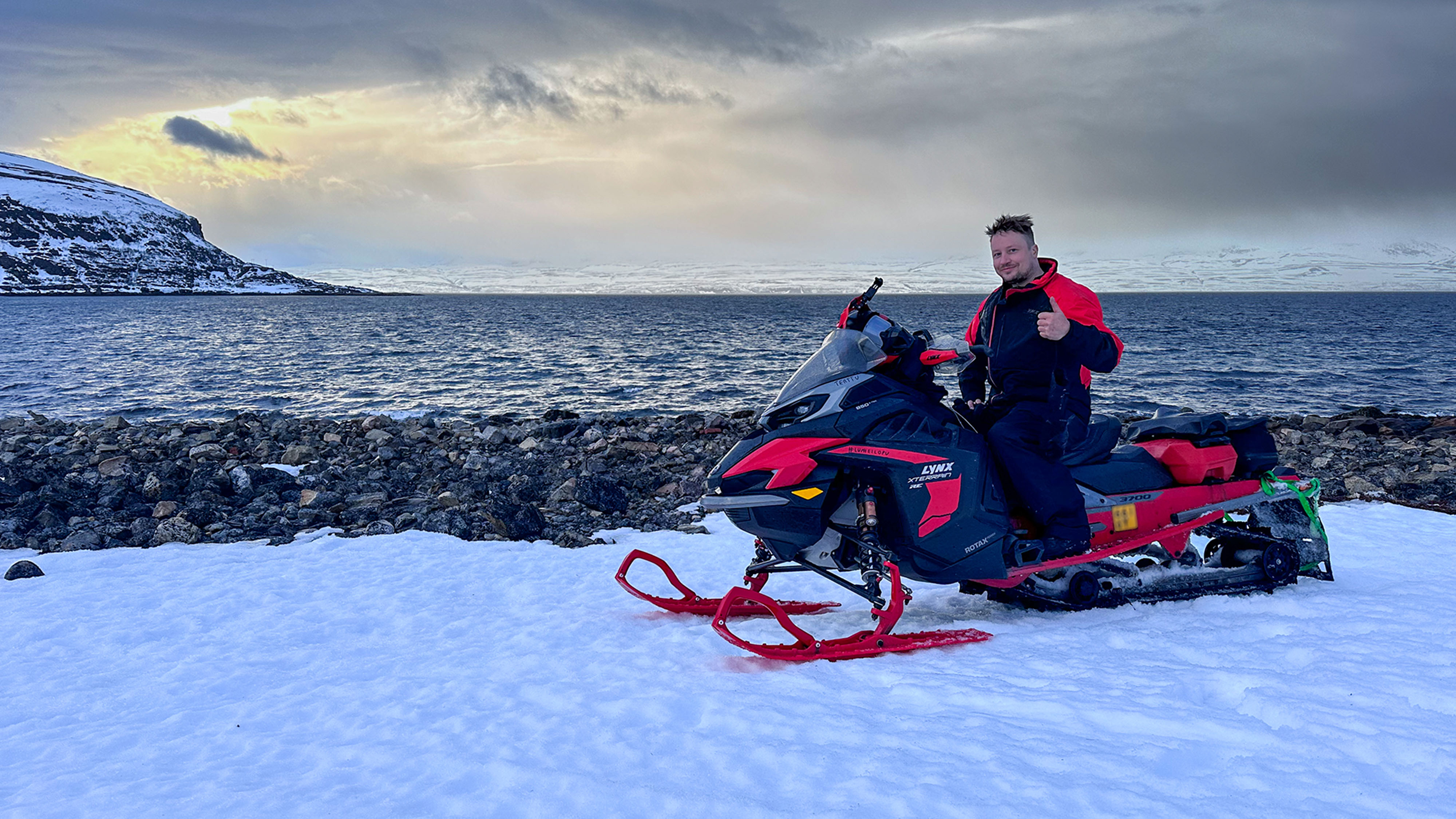 A man giving thumbs up on the shore of the Arctic Ocean on Lynx Xterrain RE 850 E-TEC crossover snowmobile