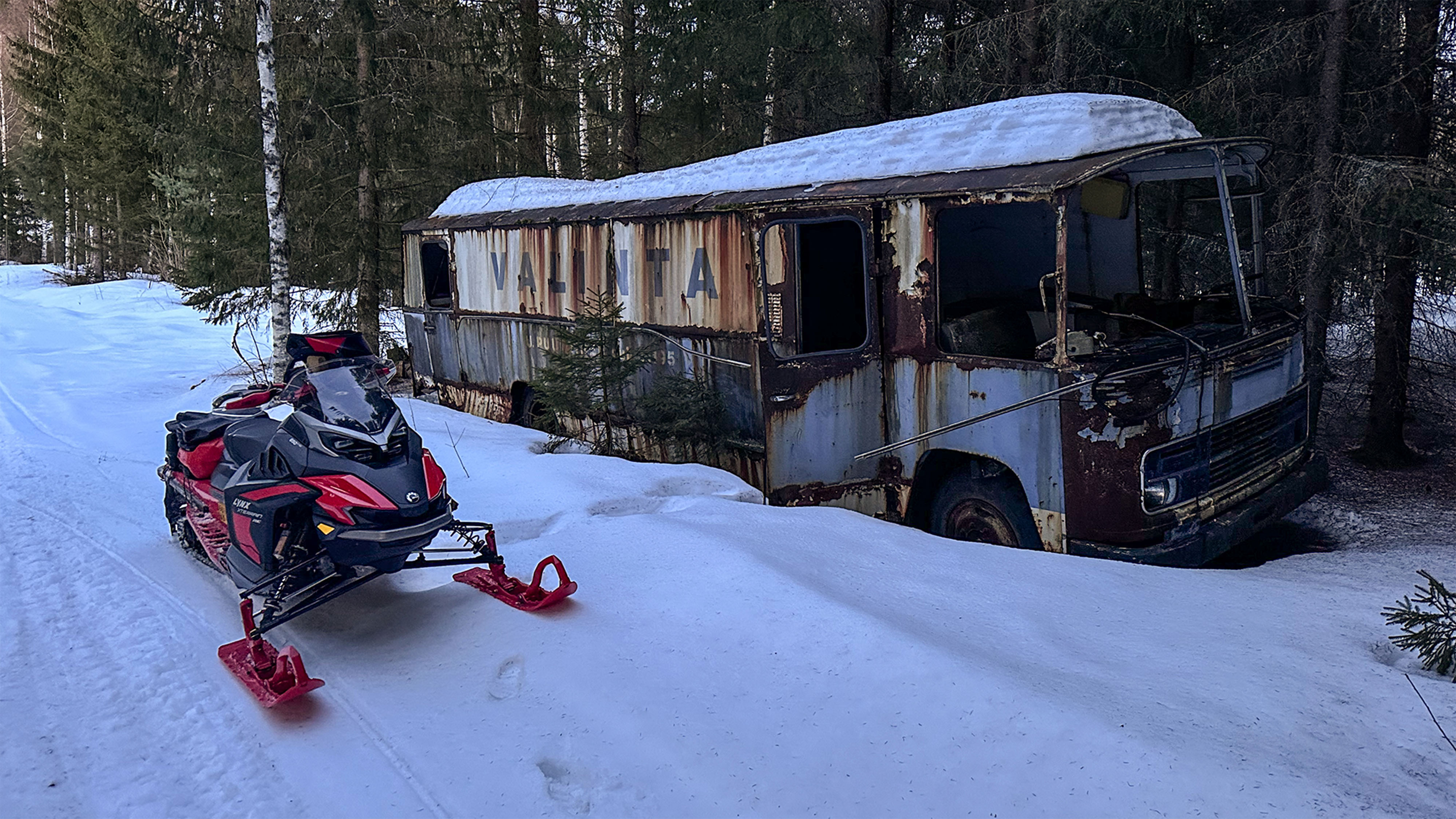 Lynx Xterrain RE 850 E-TEC crossover-snöskoter parkerad på en kälkbana bredvid ett gammalt nyttofordon