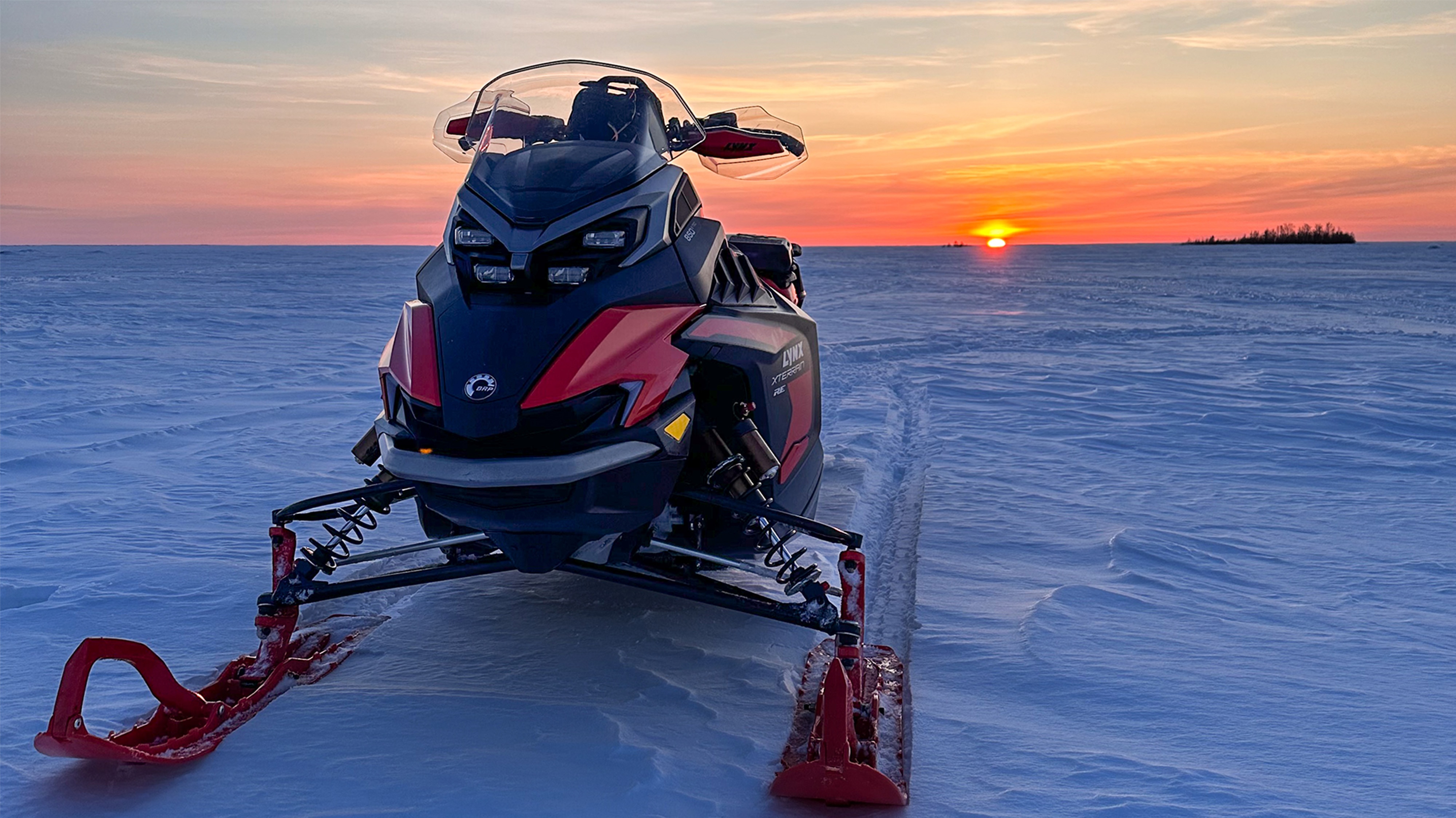 Lynx Xterrain RE 850 E-TEC crossover-snøscooter parkert på en isdekt innsjø ved solnedgang