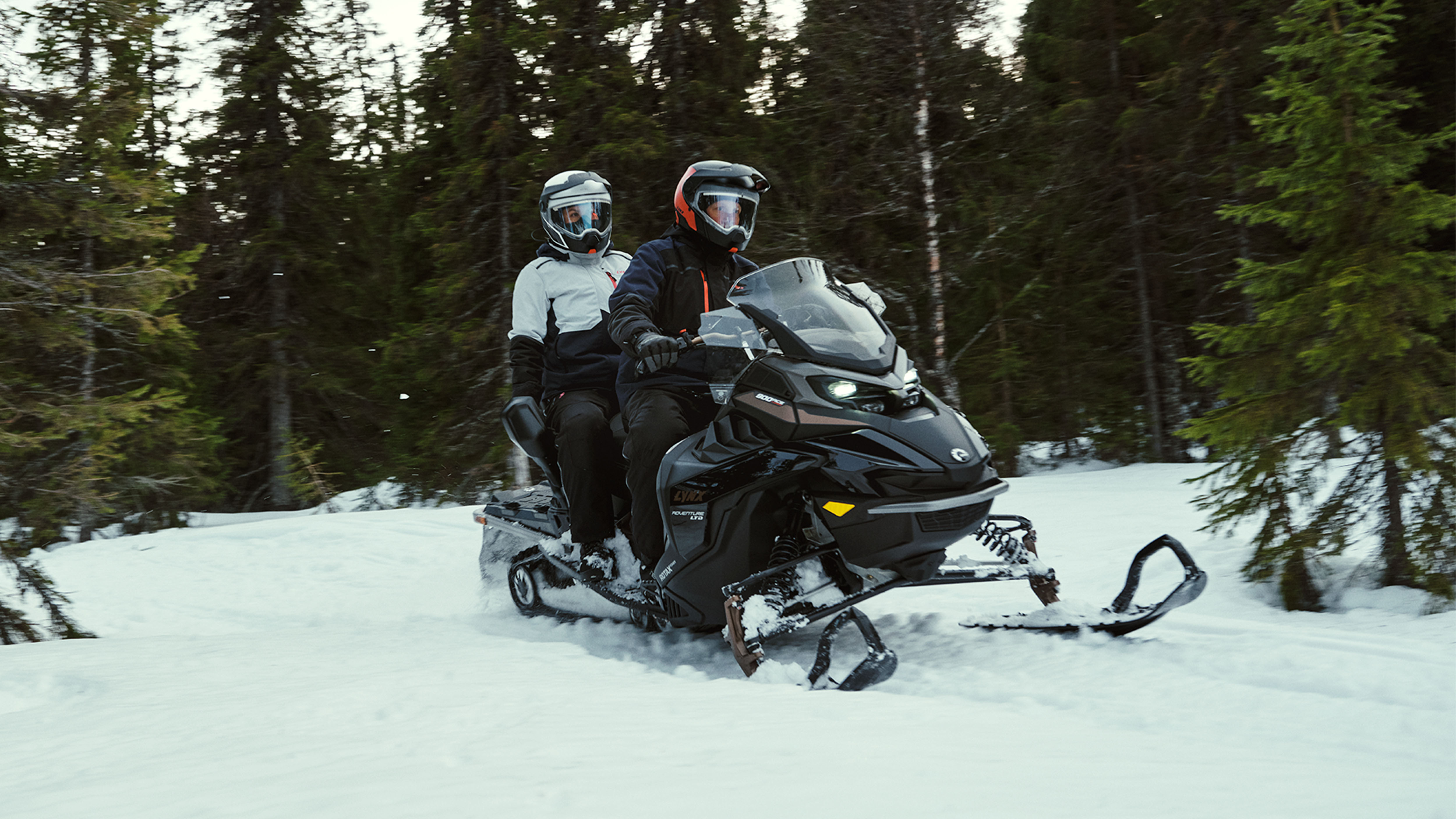 Man and woman riding together with Lynx Adventure Limited 2025 snowmobile with Passenger Kit