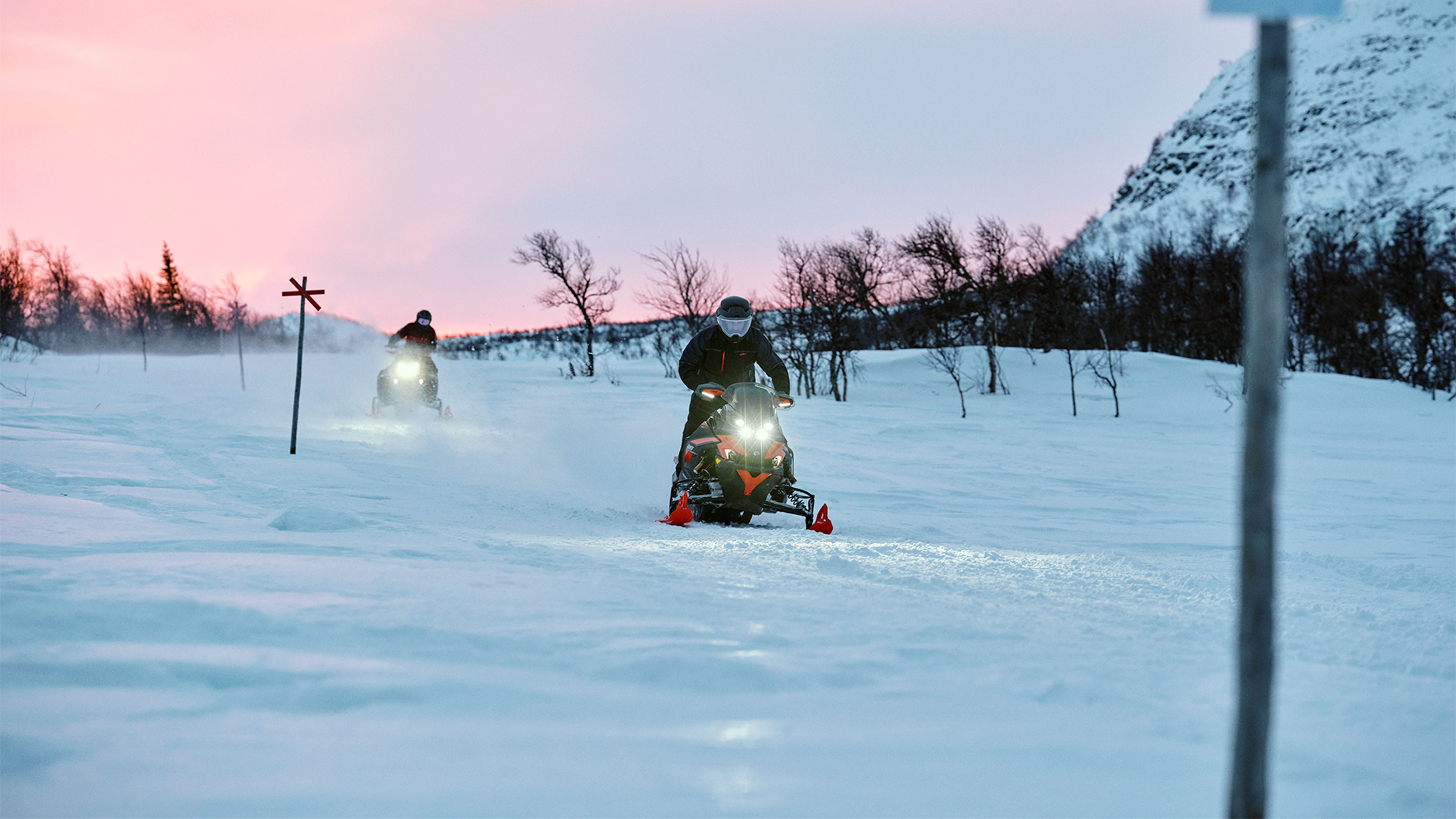 To Lynx Xterrain RE 2025-snøscootere kjører i løypen ved soloppgang.