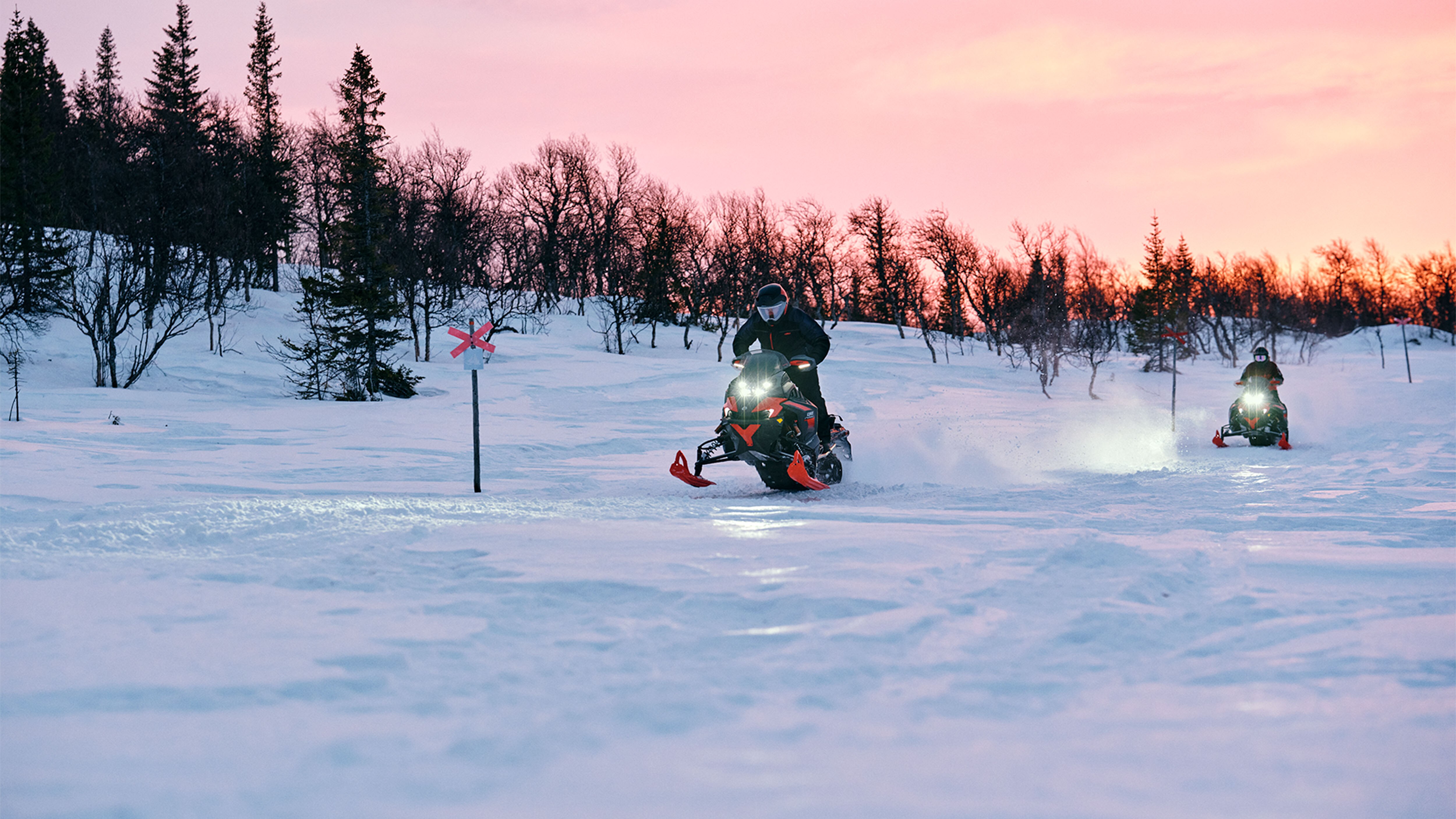 Kaksi Lynx Xterrain RE 2025 -moottorikelkkaa ajamassa reitillä auringonnousussa