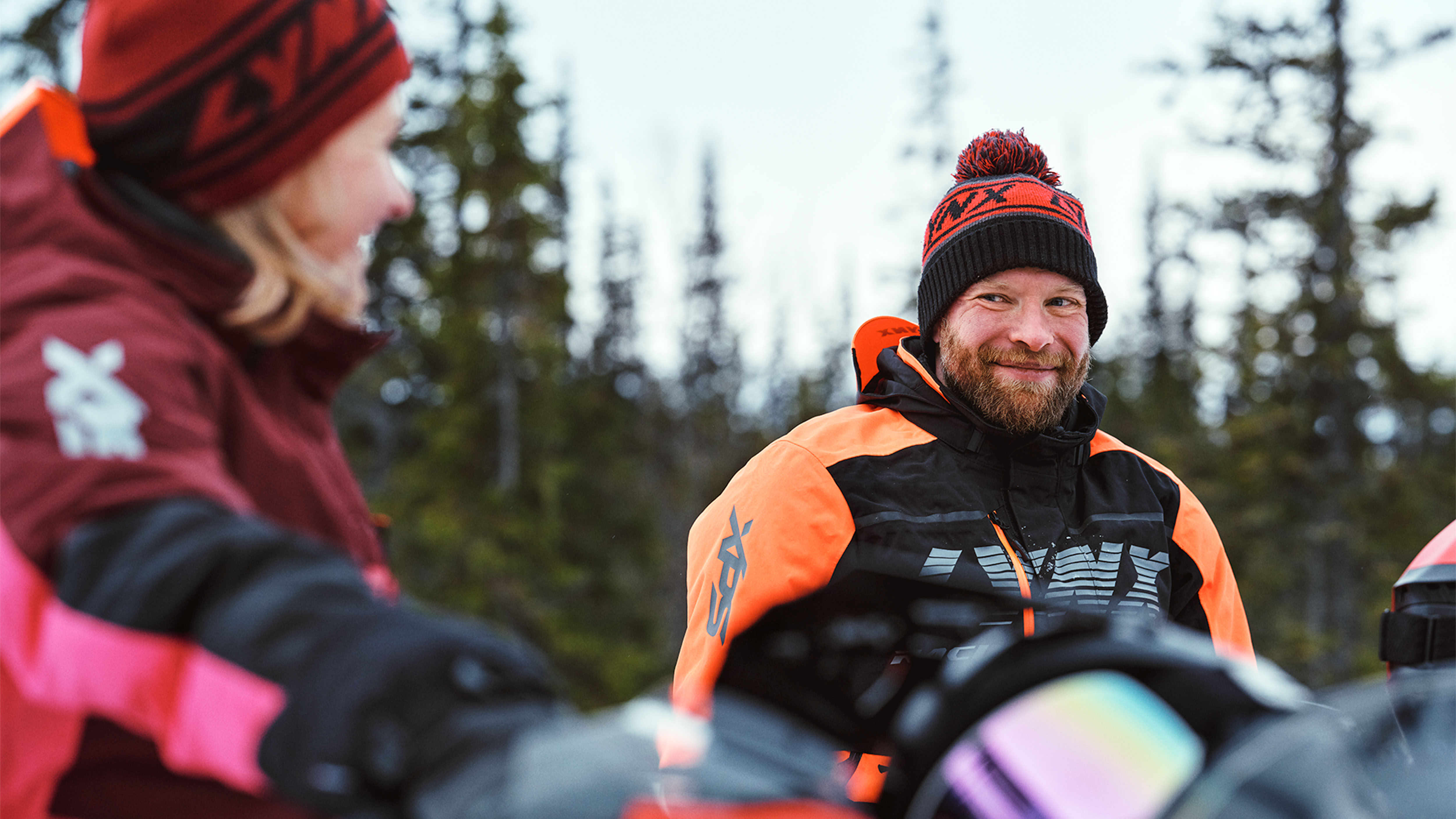 Kvinne og mann prater på snøscooter iført Lynx-kjøretøy